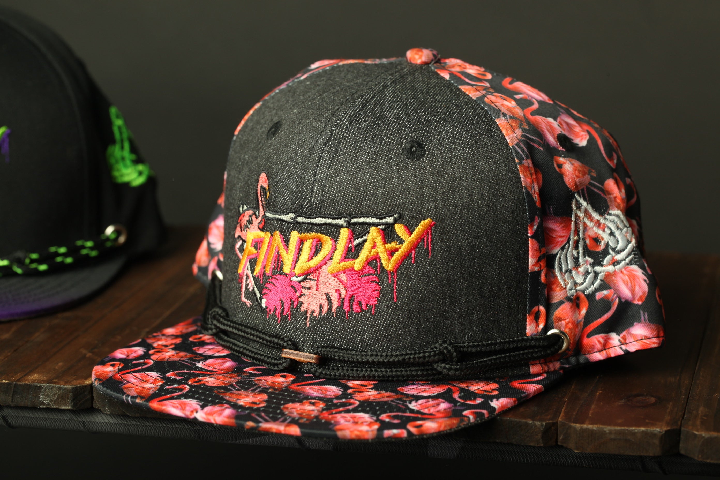 A black baseball cap with a floral pattern and the word "FINDlay" printed on it, sitting on a wooden surface.