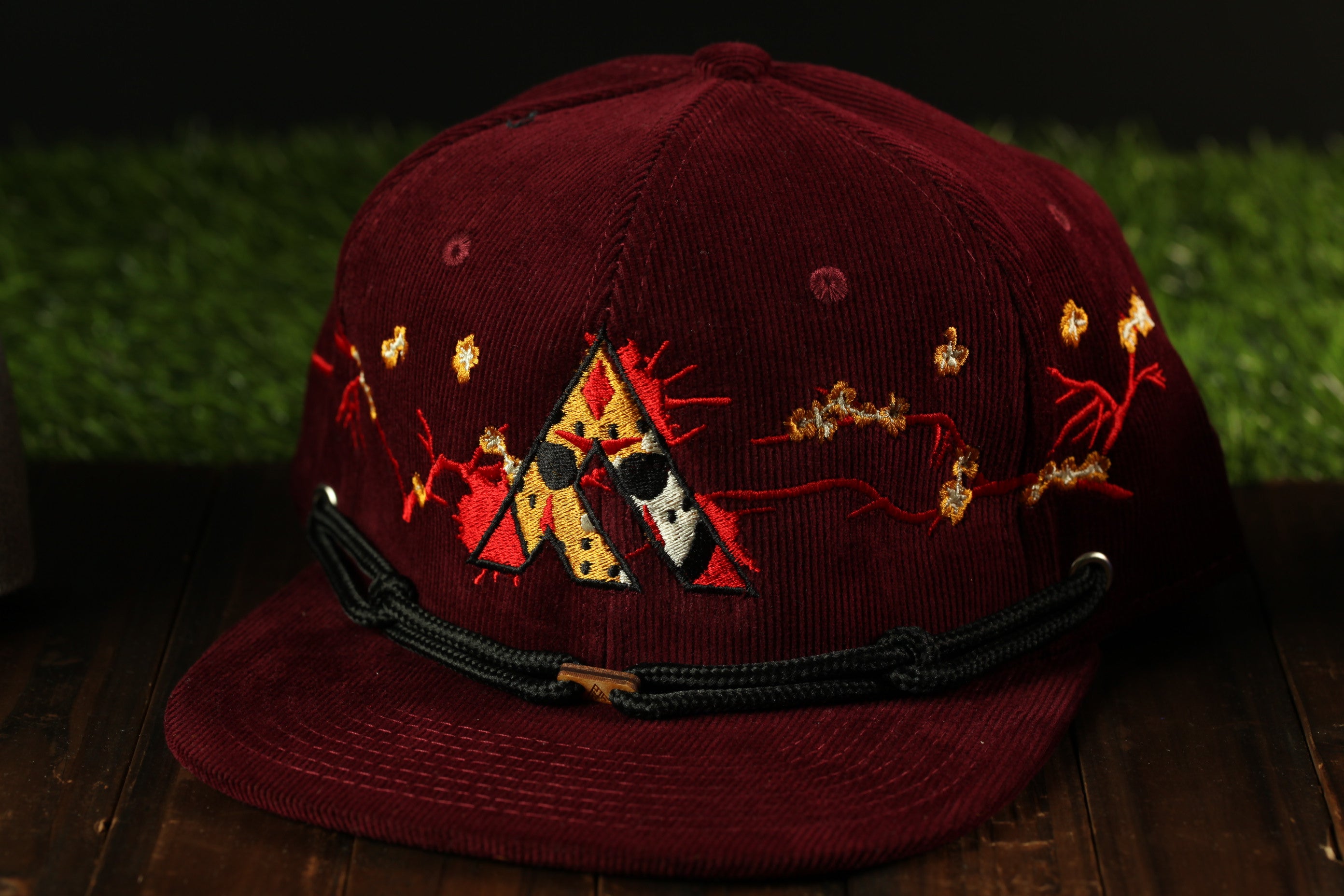 A burgundy baseball cap with a black band and embroidered designs on the front.