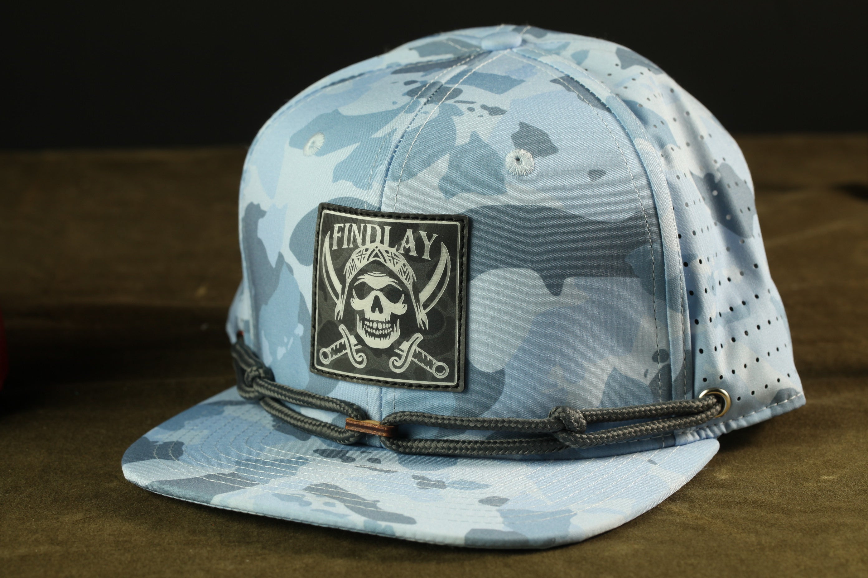 A camouflage baseball cap with a skull patch and the text "FIND LAY" printed on it.
