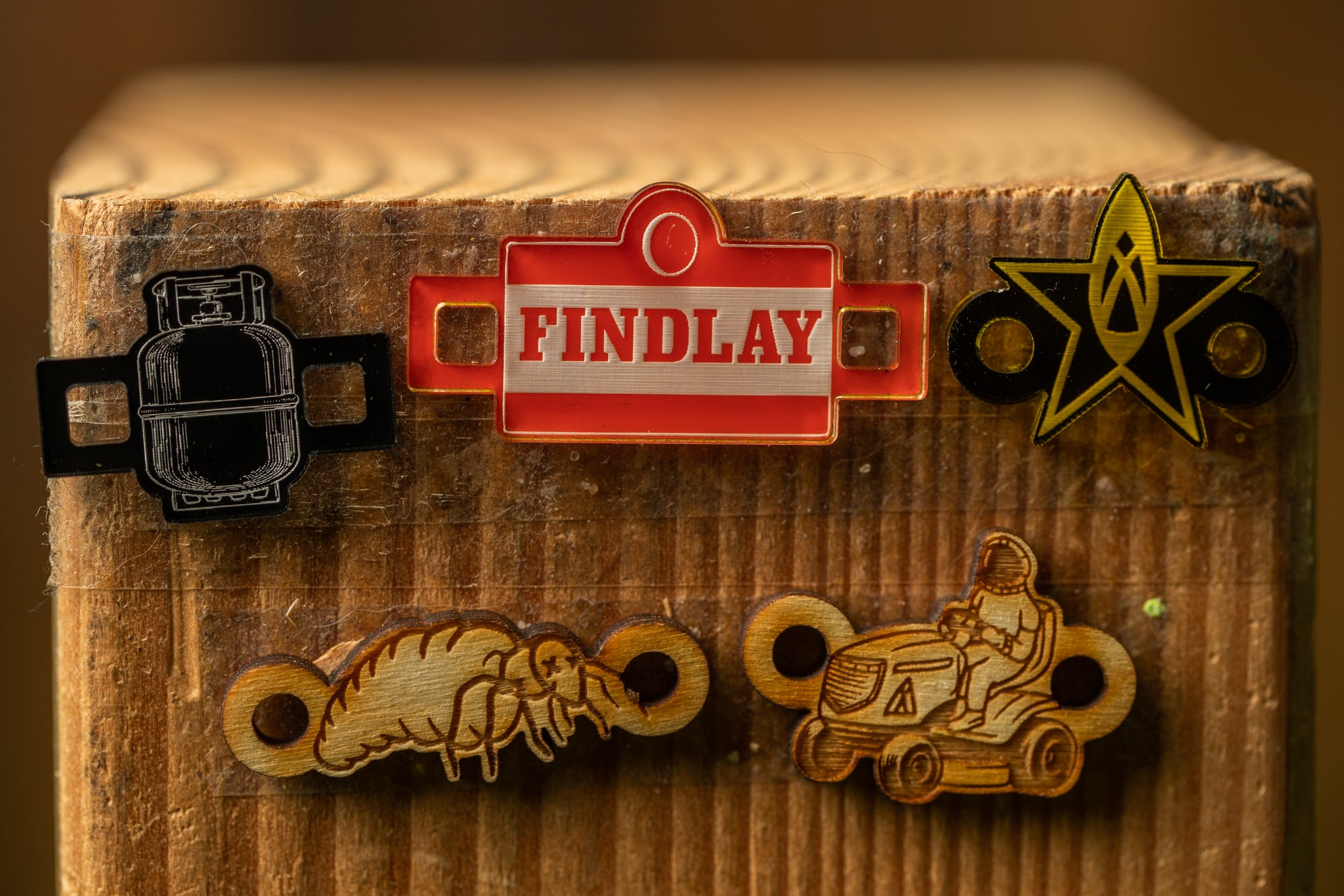 a wooden surface with various objects attached to it, including a red and white sign, a black and white drawing of a gas cylinder, a yellow star, and a wooden tractor with a person on it.