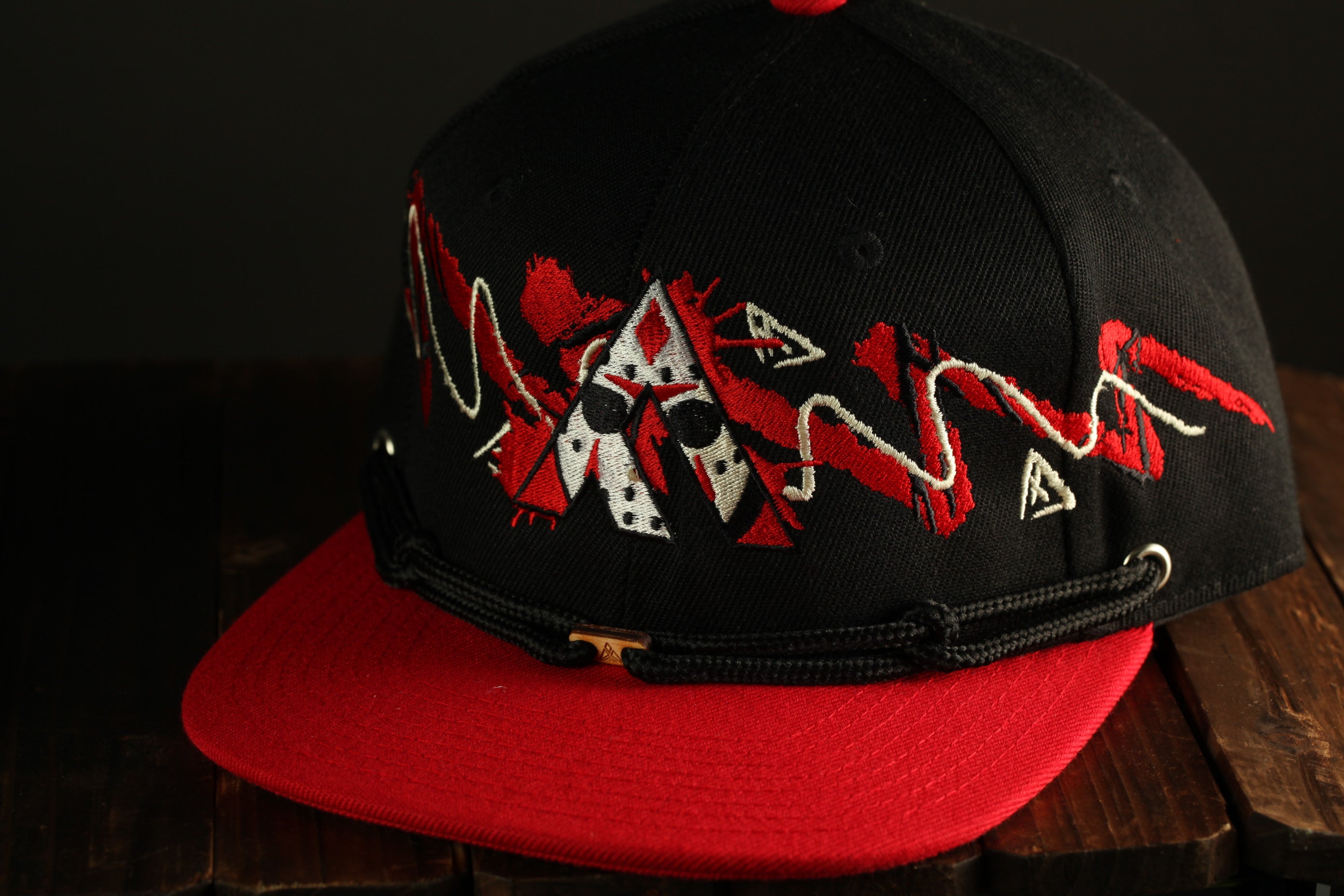 A black baseball cap with red and white embroidered designs, placed on a wooden surface.