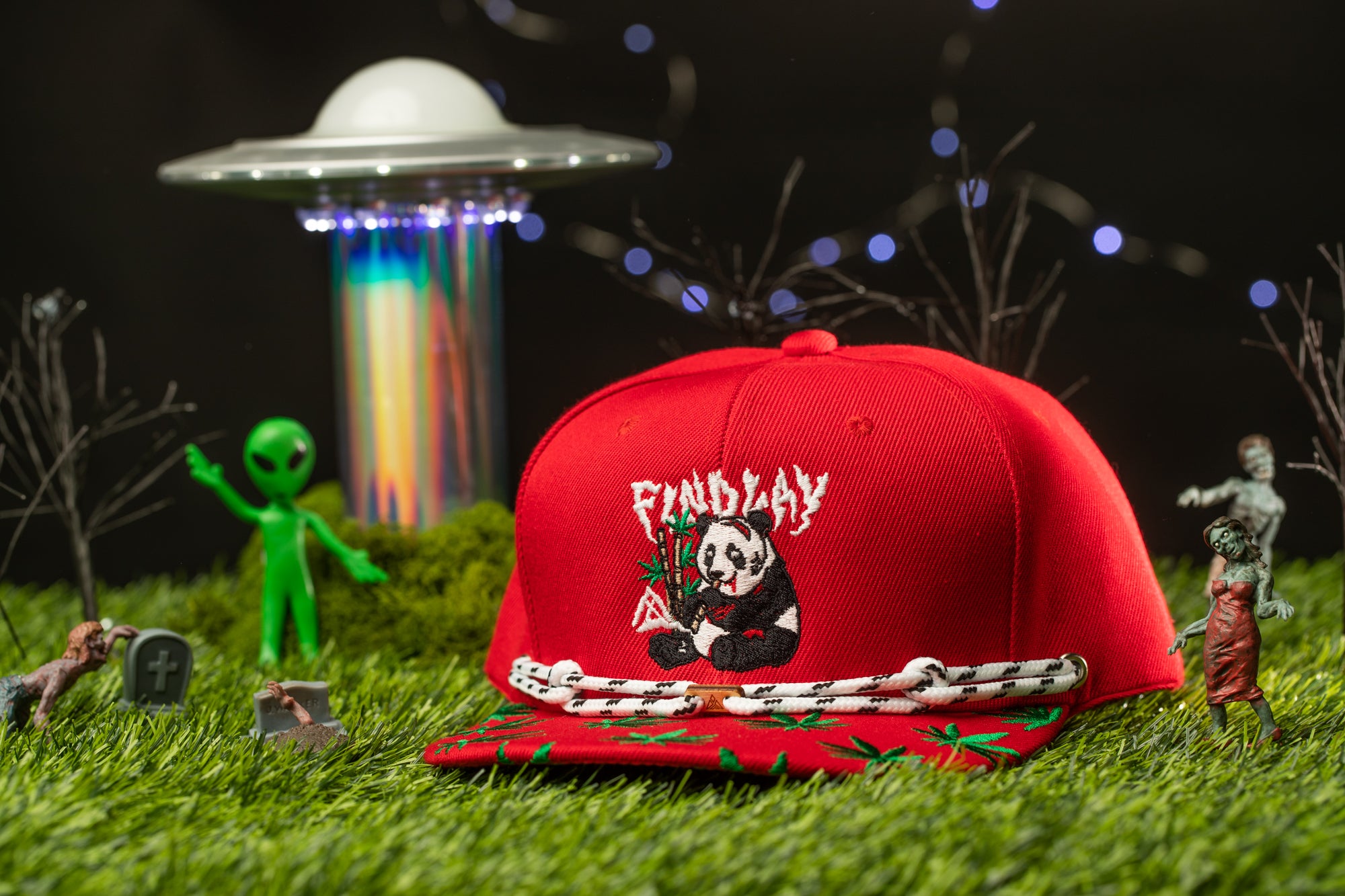 a red baseball cap with a panda bear design, surrounded by various toys and figurines, including a green alien figure, a zombie, and a spaceship.