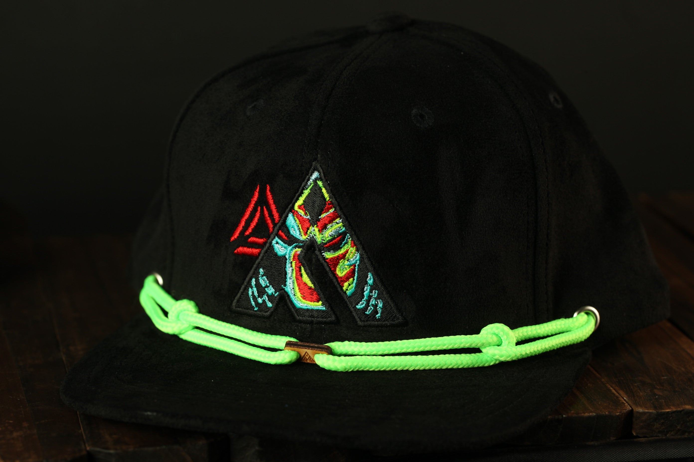 A black baseball cap with a colorful, abstract design on the front, featuring a triangle and a colorful, abstract pattern.