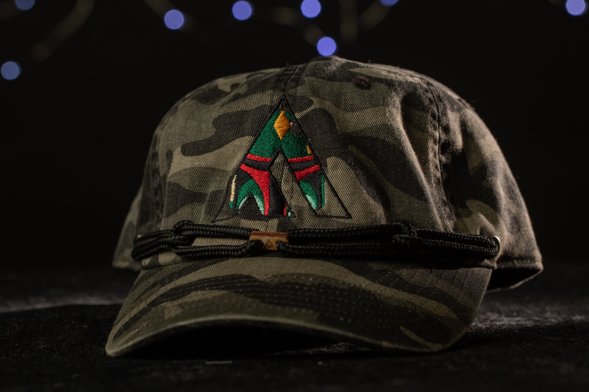 A camouflage baseball cap with a colorful embroidered logo on the front.