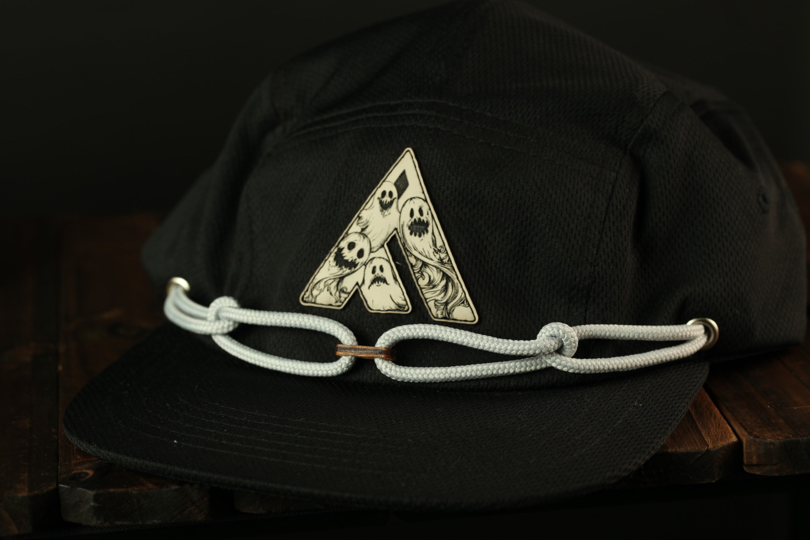 A black baseball cap with a white rope strap and a graphic design on the front.