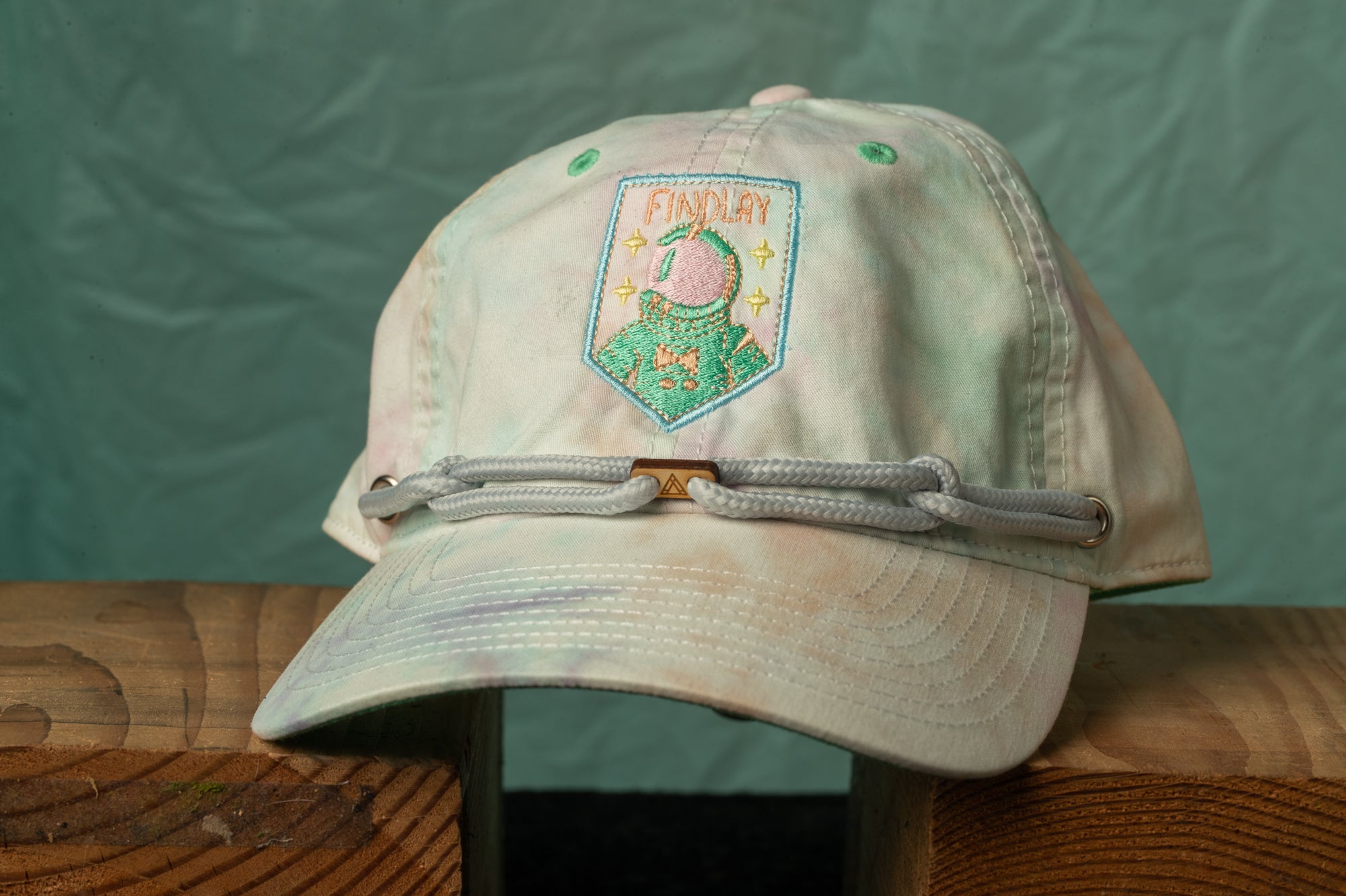 A tie-dye baseball cap with a small embroidered patch on the front, featuring a cartoon character and the word "FINDlay".