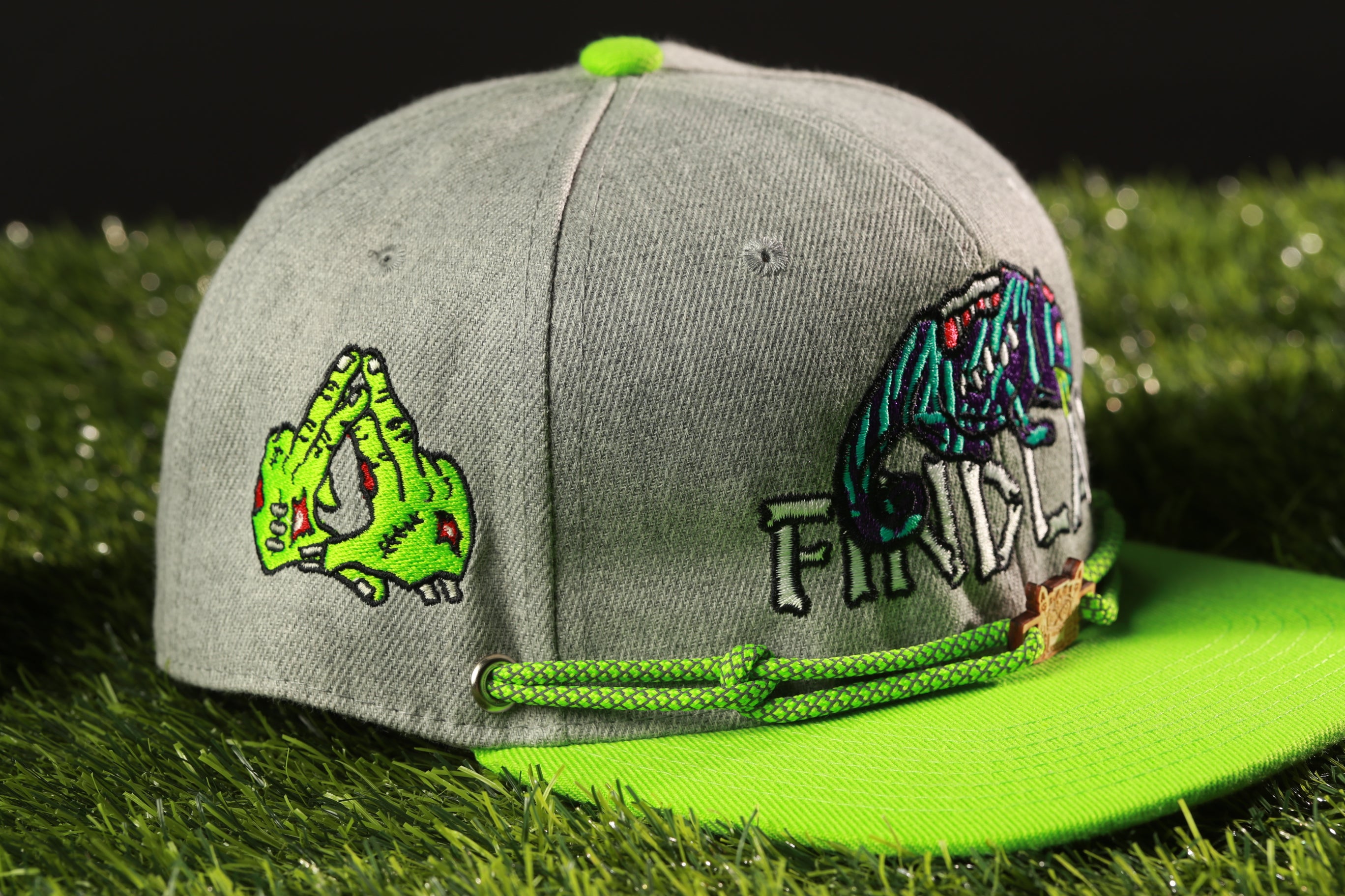 A grey baseball cap with a green brim and a green string, featuring a graphic of a green zombie hand and the word "FRIDAY" printed on it.