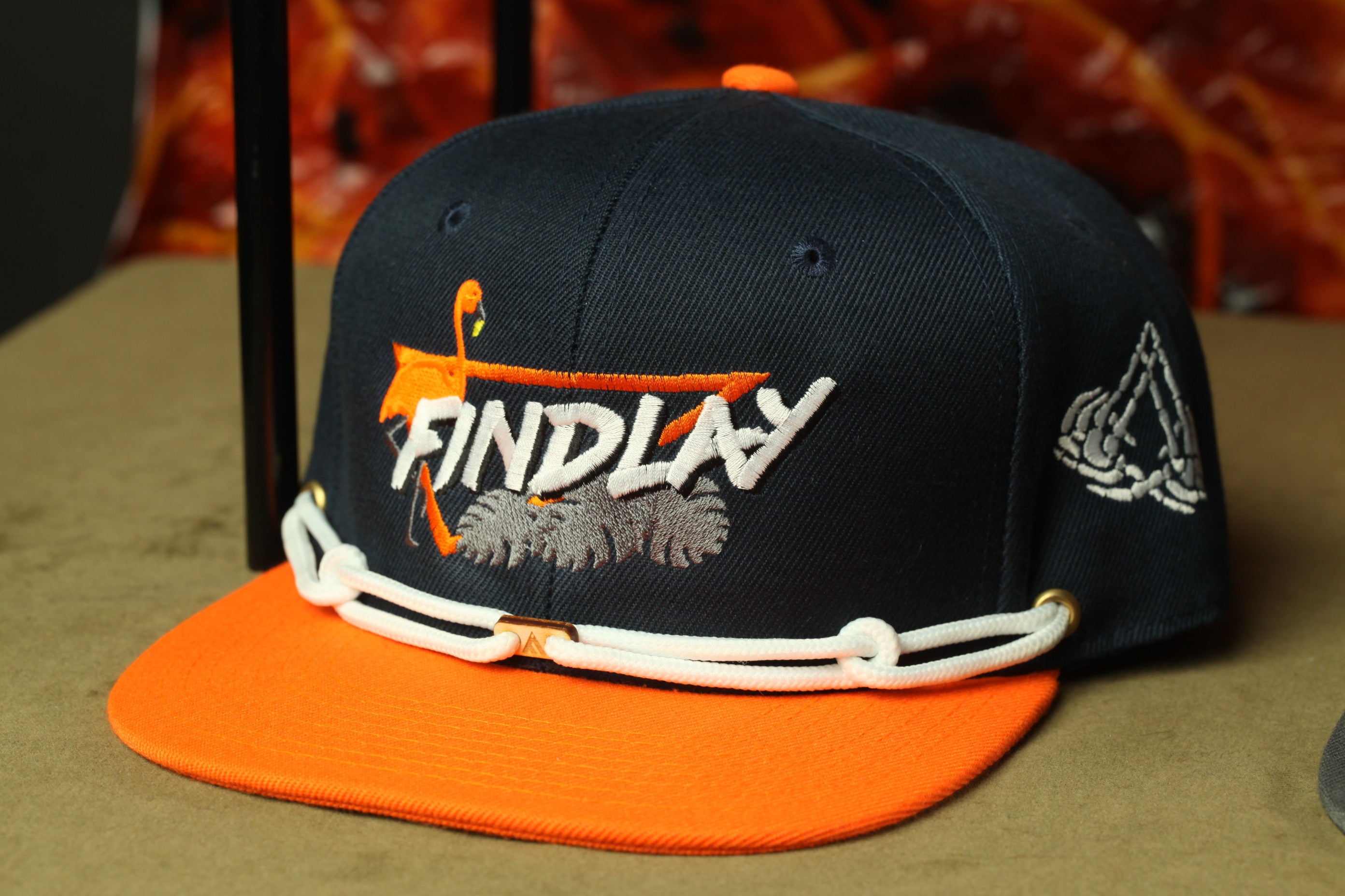 A navy blue baseball cap with an orange brim and white text on the front, sitting on a brown surface.