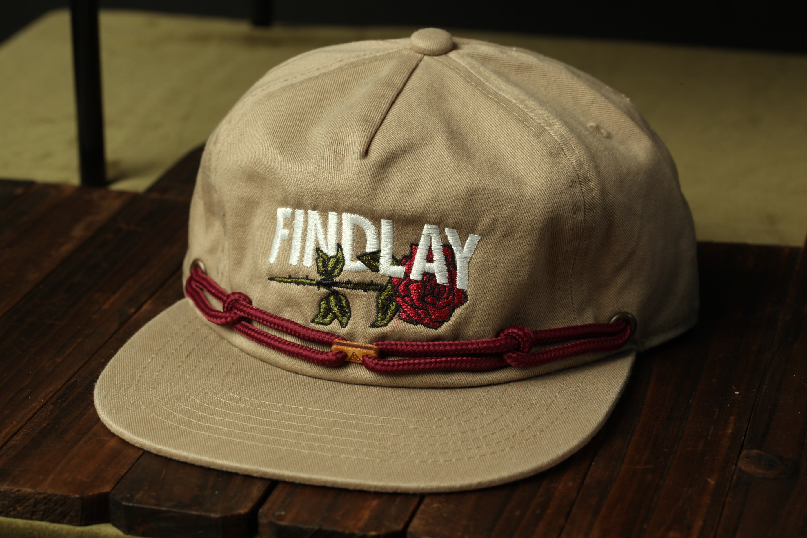 A beige baseball cap with the word "FINDlay" embroidered on it, sitting on a wooden surface.