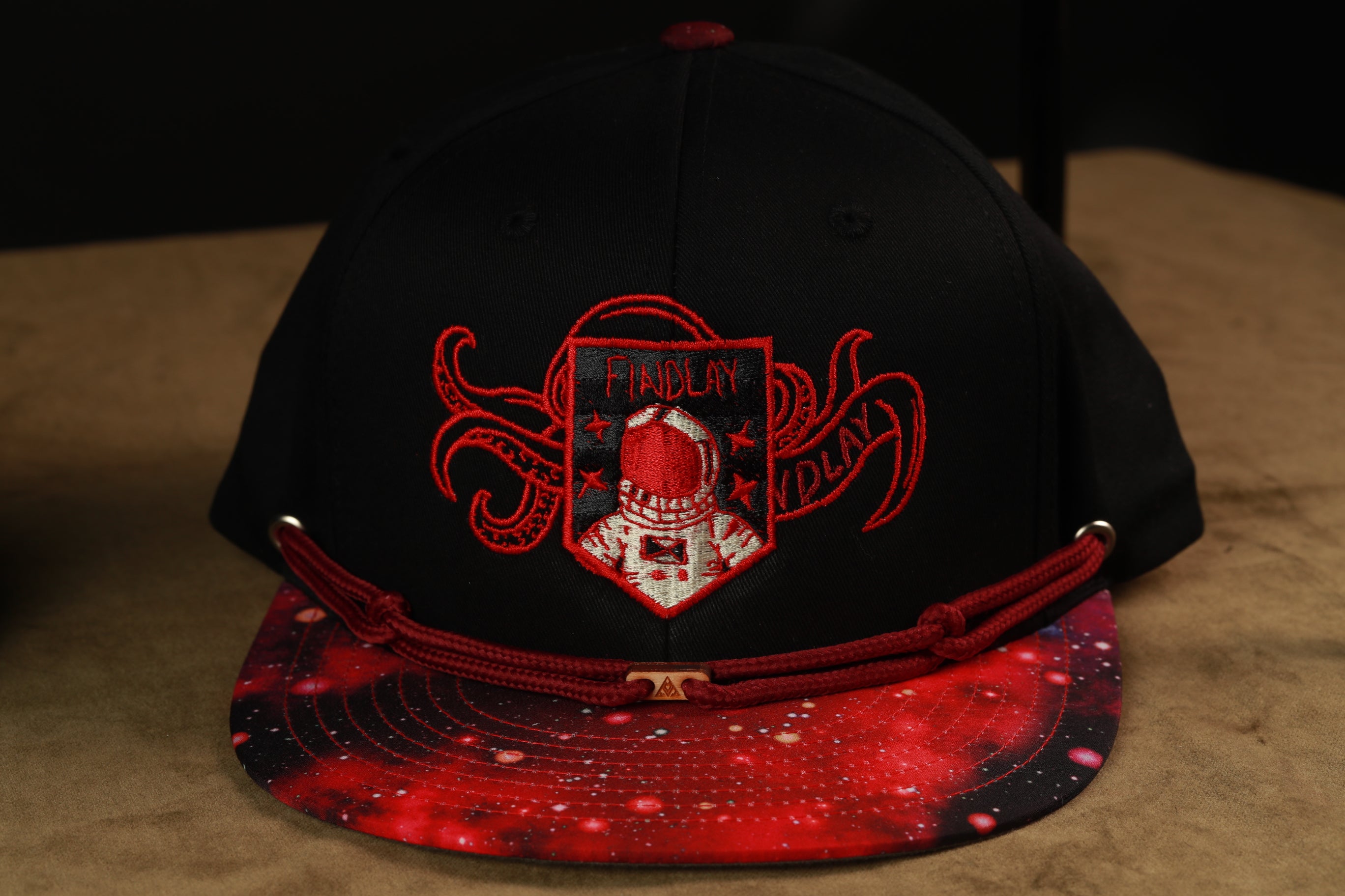 A black baseball cap with a red and white design, featuring a red and white emblem with a red helmet and the text "FINITY" and "DUNGE" on it.