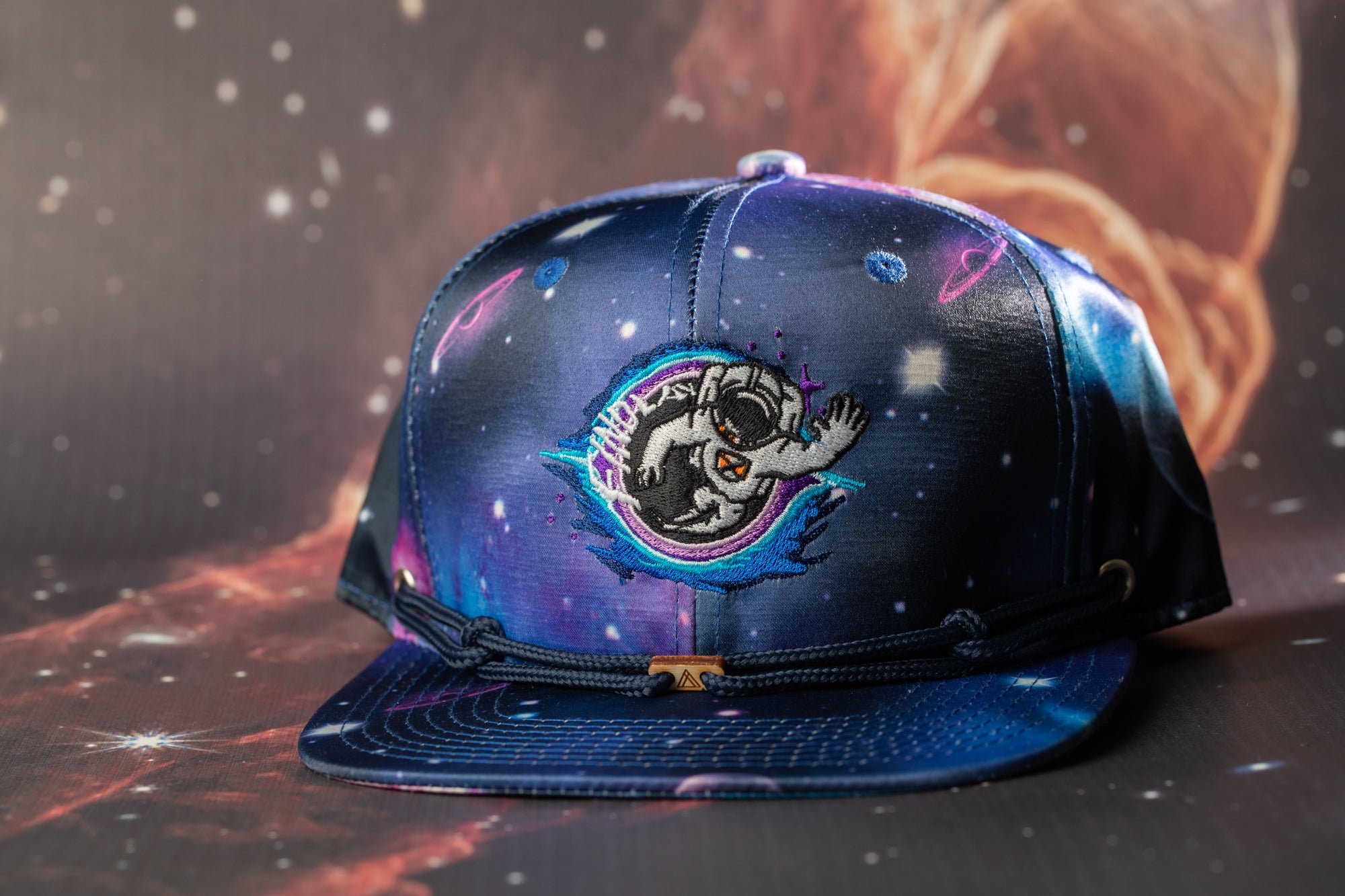 A blue baseball cap with a space-themed design, featuring a graphic of a person in a spacesuit and a planet.