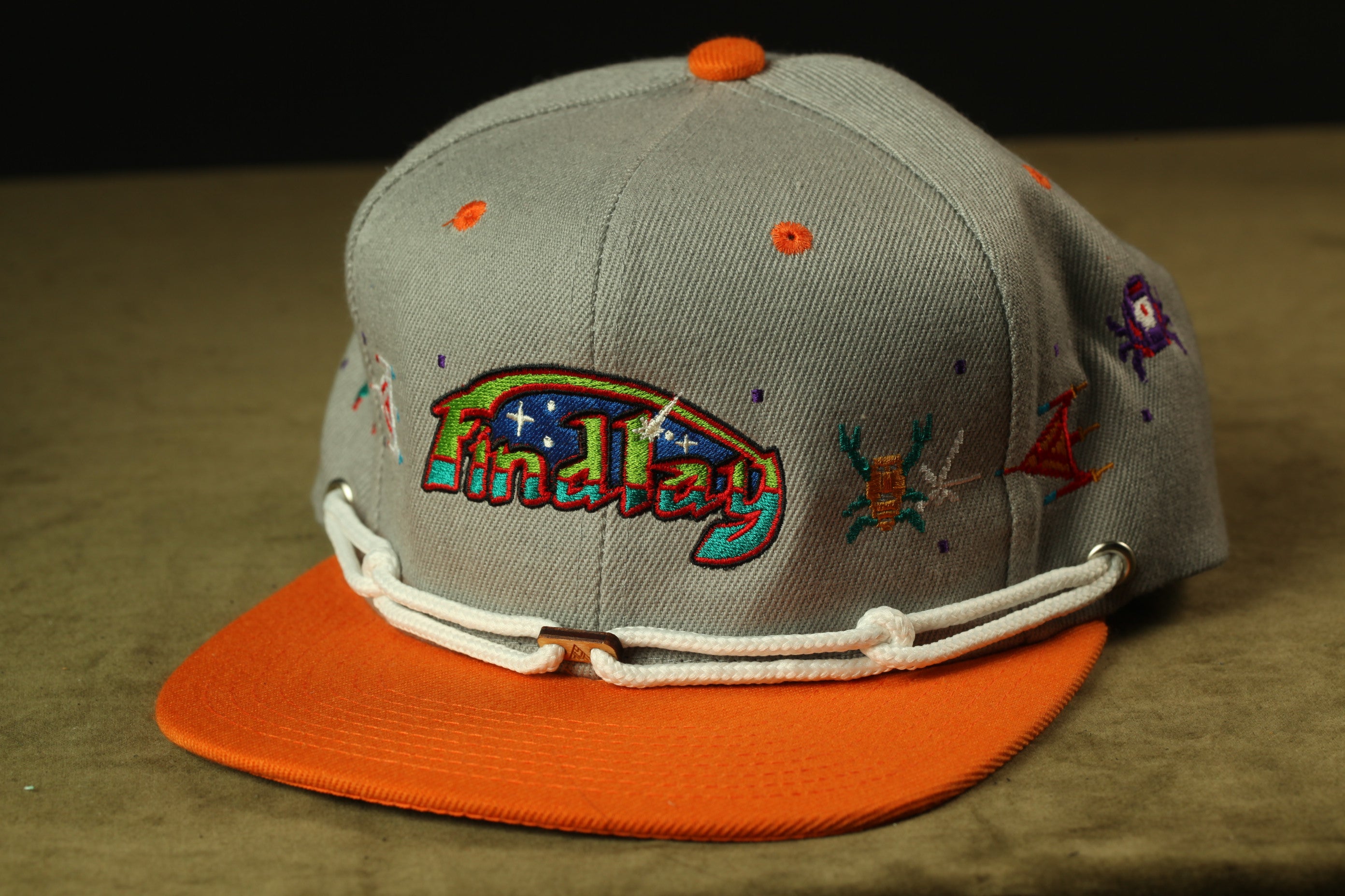 A gray baseball cap with an orange brim, adorned with colorful embroidered designs and the word "Findlay" printed on it.
