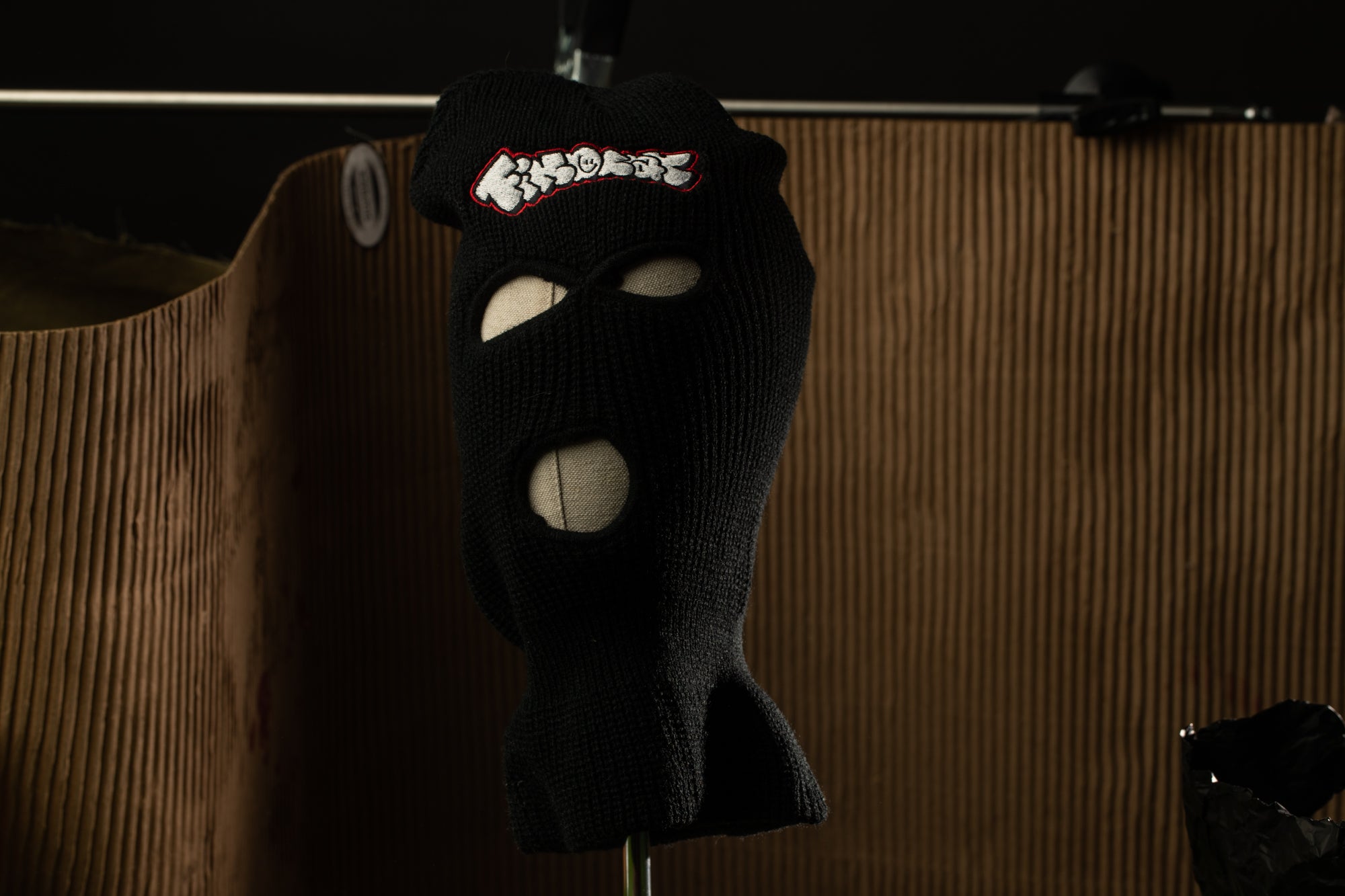 A black ski mask with a white logo on the front, hanging on a rack.
