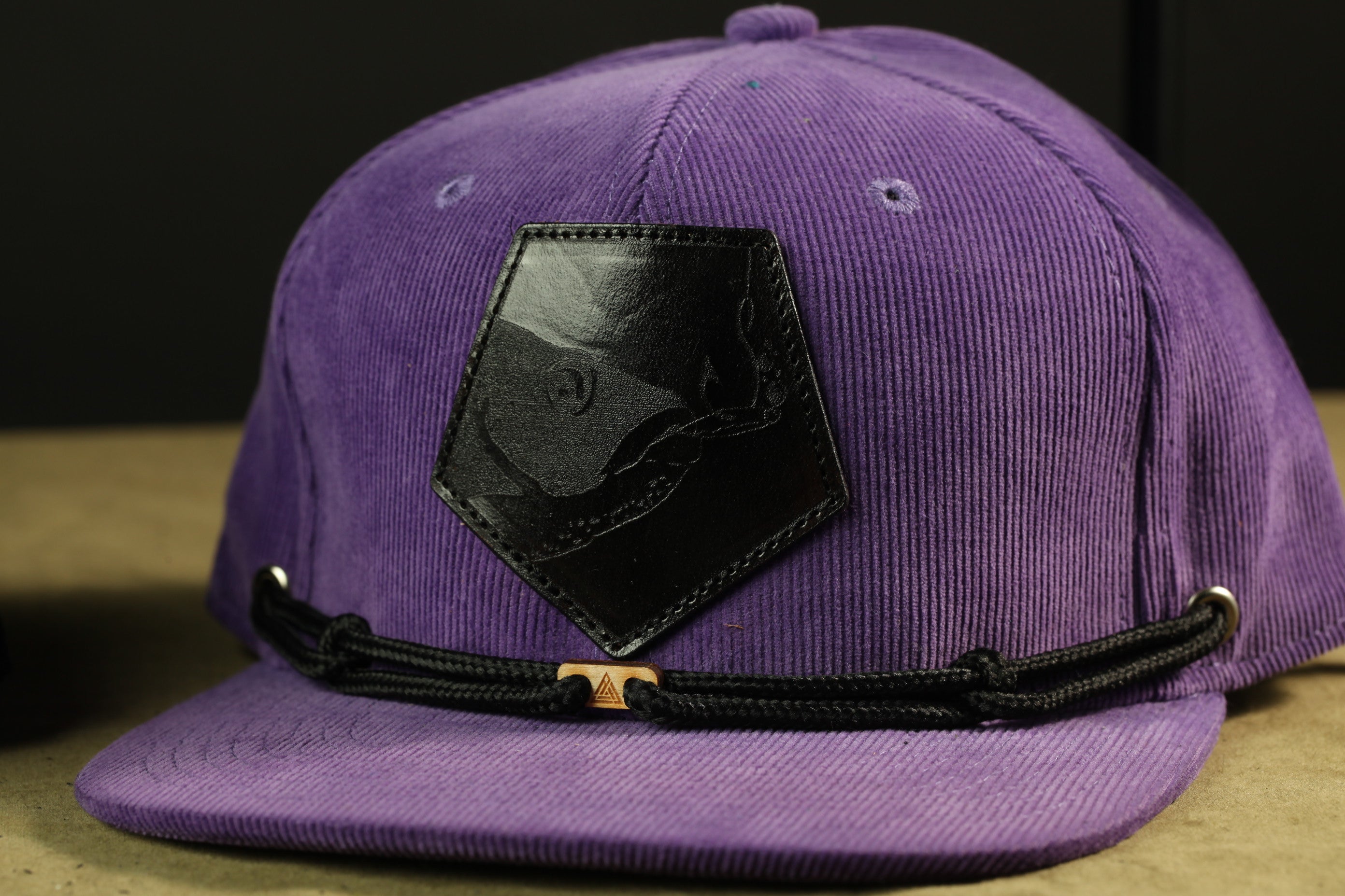 A purple baseball cap with a black leather patch and a black strap.