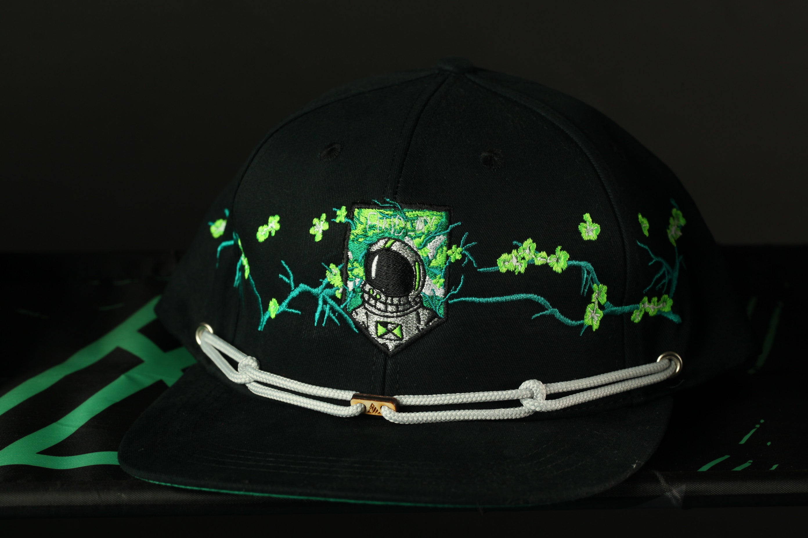 A black baseball cap with a green and white floral design and a silver metal buckle.