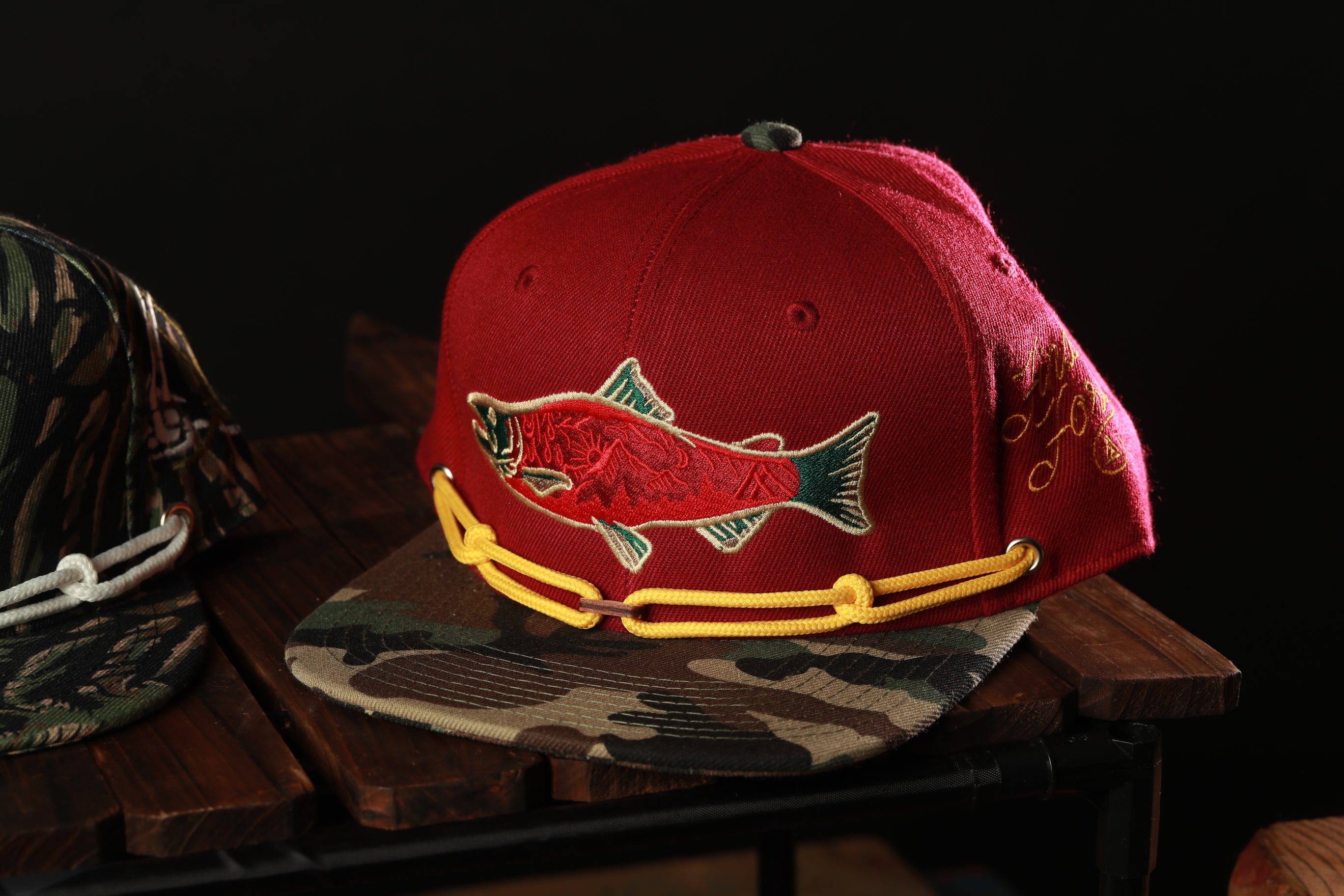 A red baseball cap with a fish embroidered on it, placed on a wooden surface.