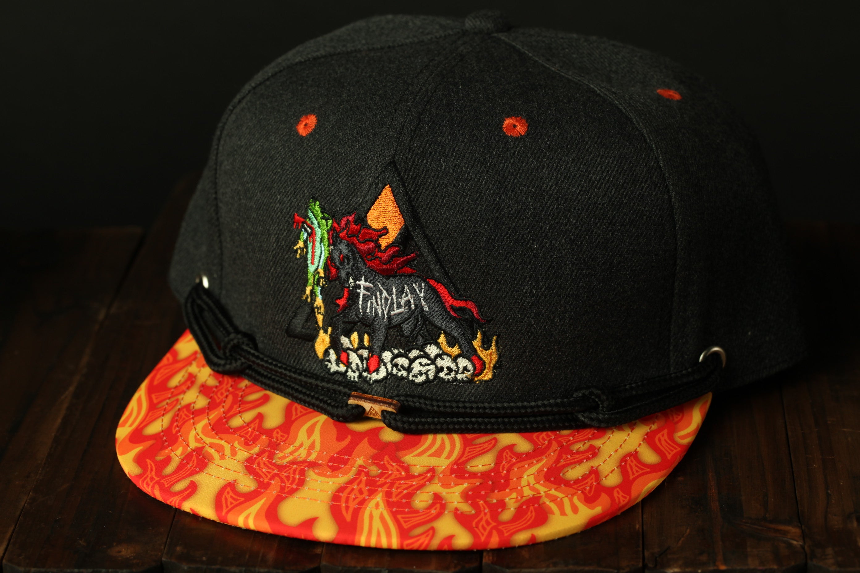 A black baseball cap with a vibrant, fiery pattern on the brim and a small embroidered design on the front.