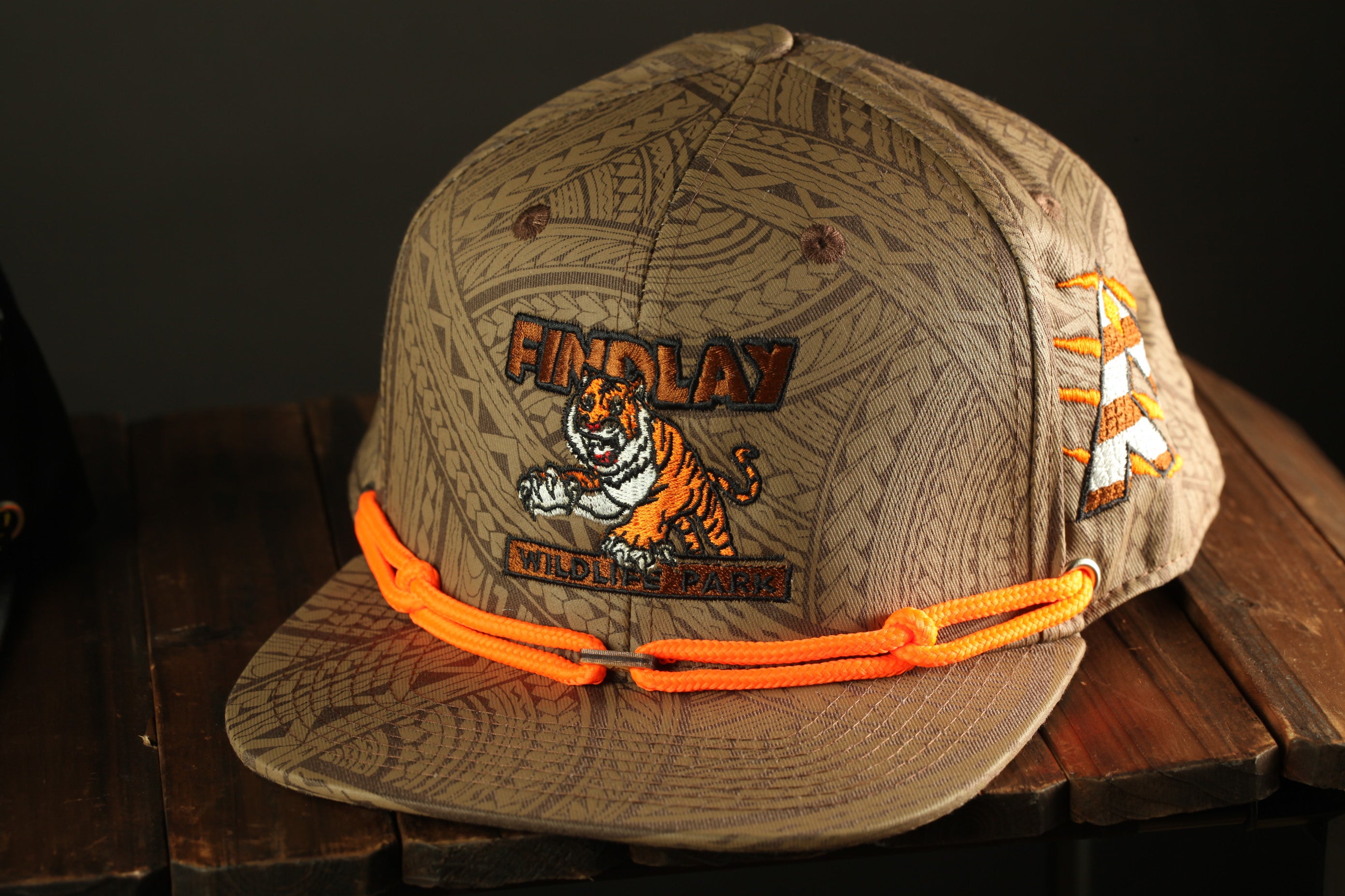 A tan baseball cap with a tiger graphic and the text "FIND LAY" printed on it, sitting on a wooden surface.
