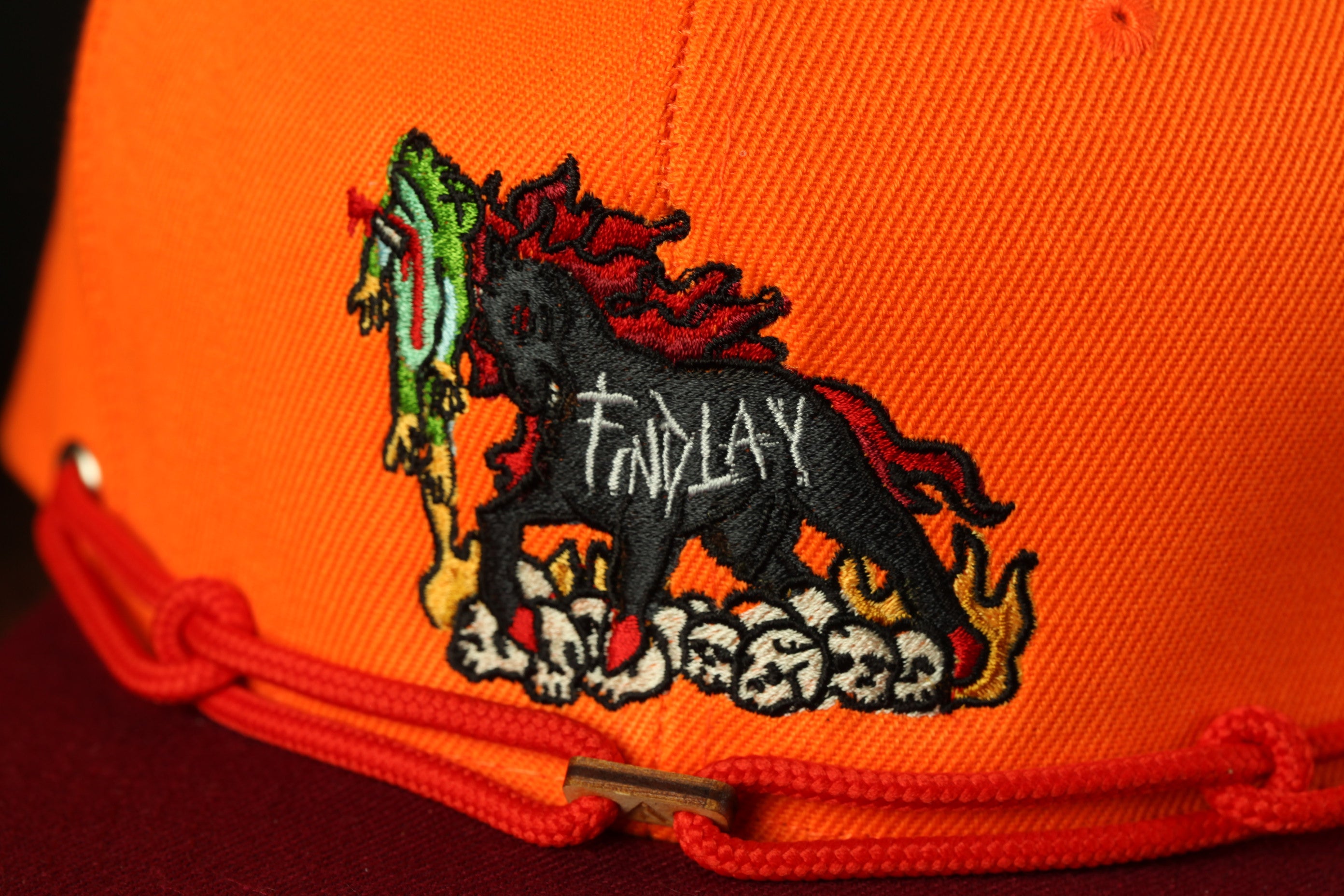 a close-up view of a bright orange baseball cap with a detailed embroidered design on the front.
