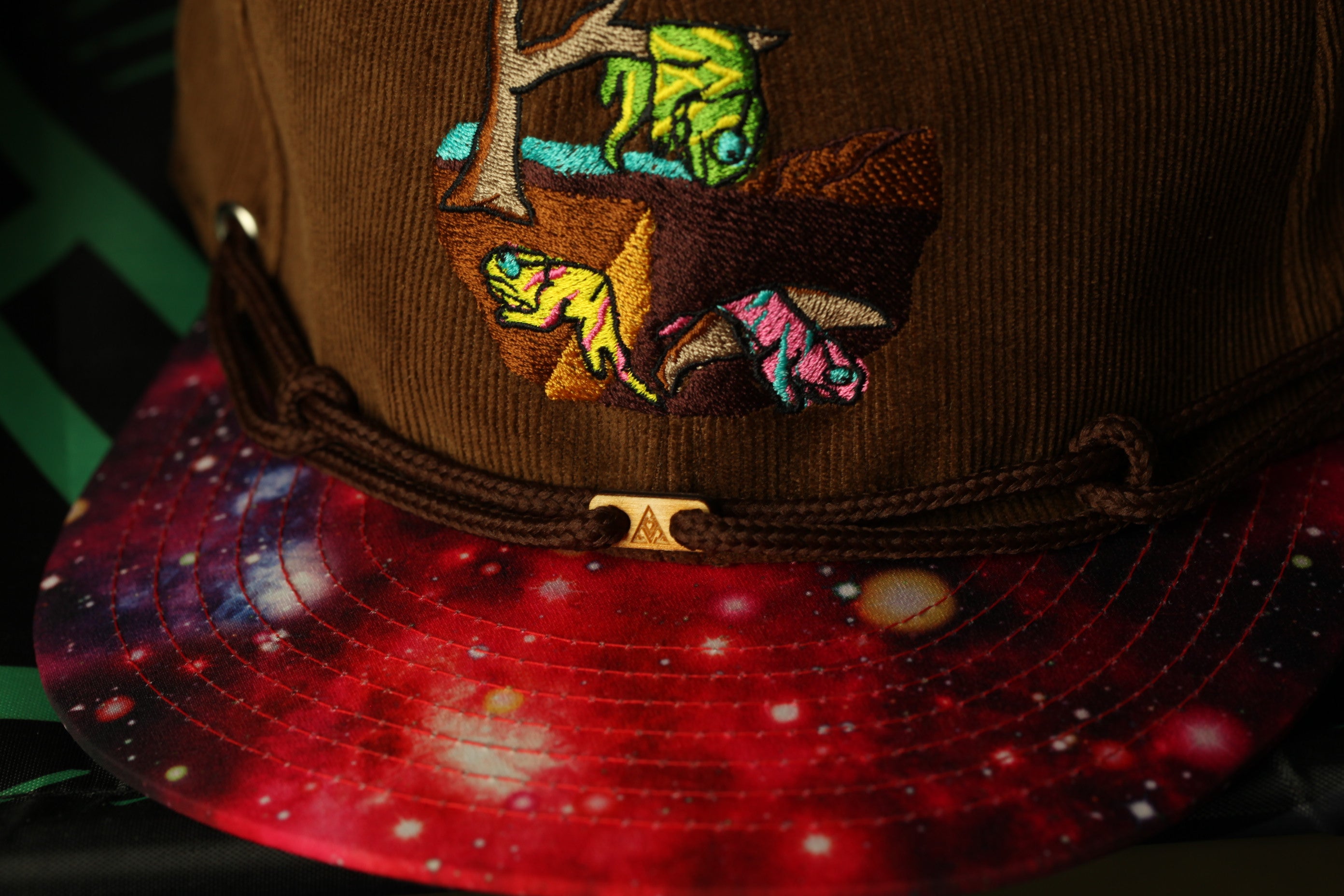 A close-up view of a brown baseball cap with a colorful, space-themed design on the front.