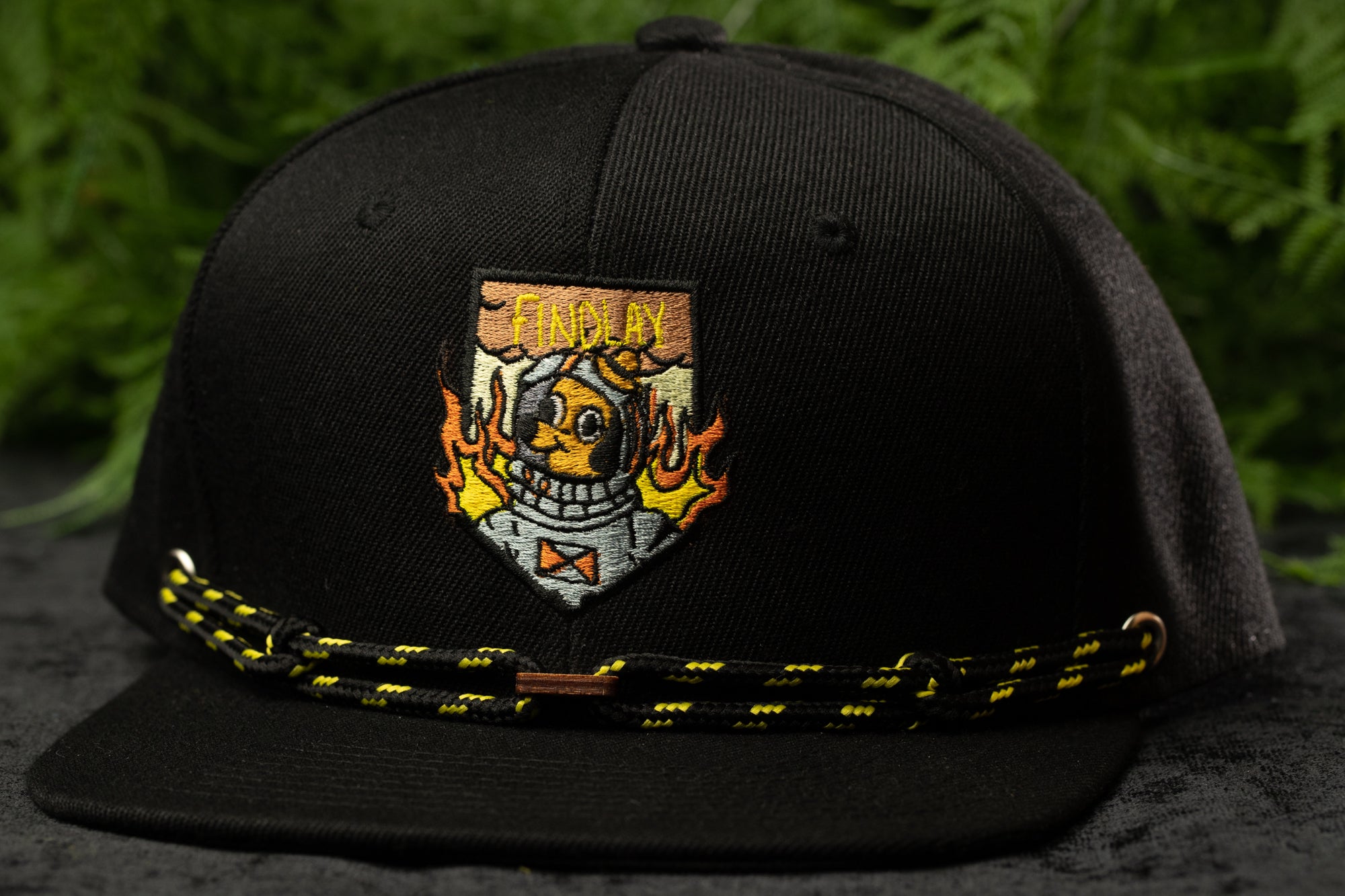 A black baseball cap with a colorful, cartoonish design on the front, featuring a flame-like element and a character wearing a helmet.