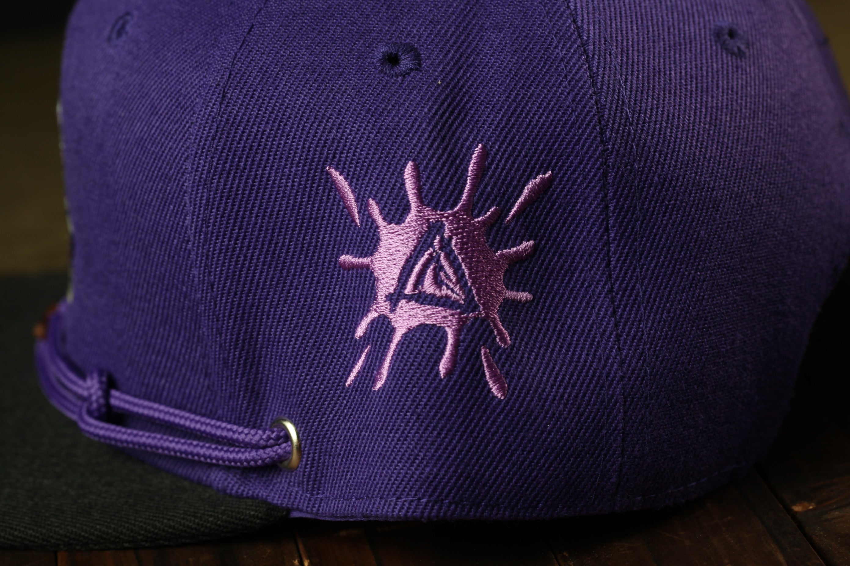 A close-up view of a purple baseball cap with a unique embroidered design on the front.