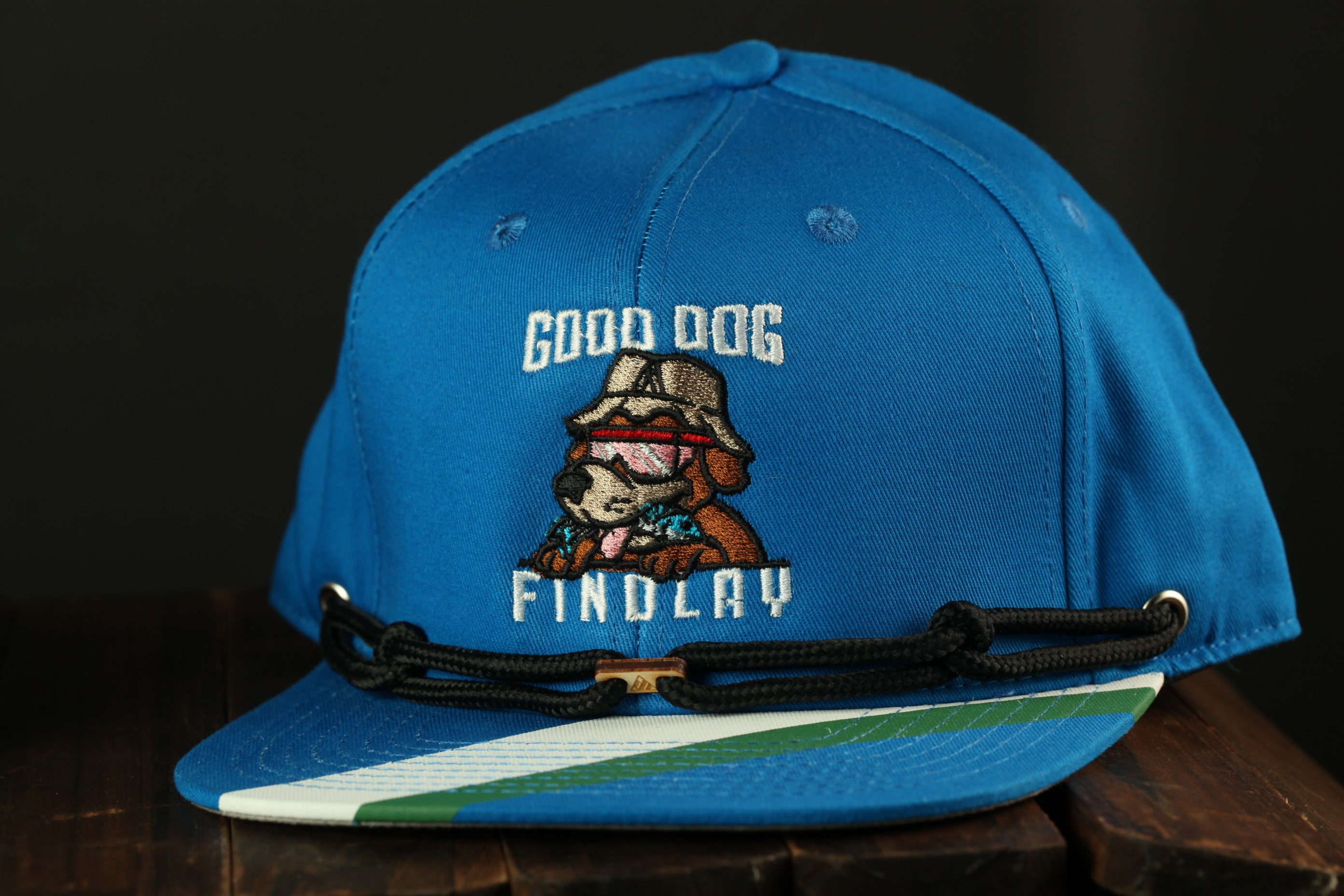 A blue baseball cap with a cartoon dog and the text "GOOD DOG FINDlay" printed on it.