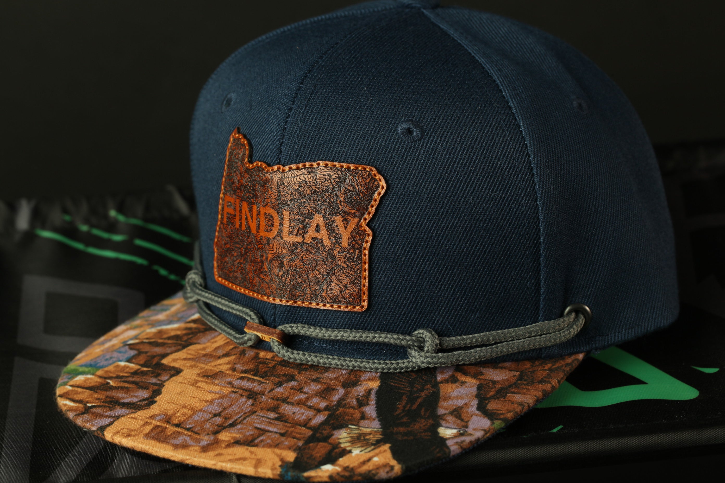 A navy blue baseball cap with a camouflage pattern and a patch that says "FINDLAY" on it.