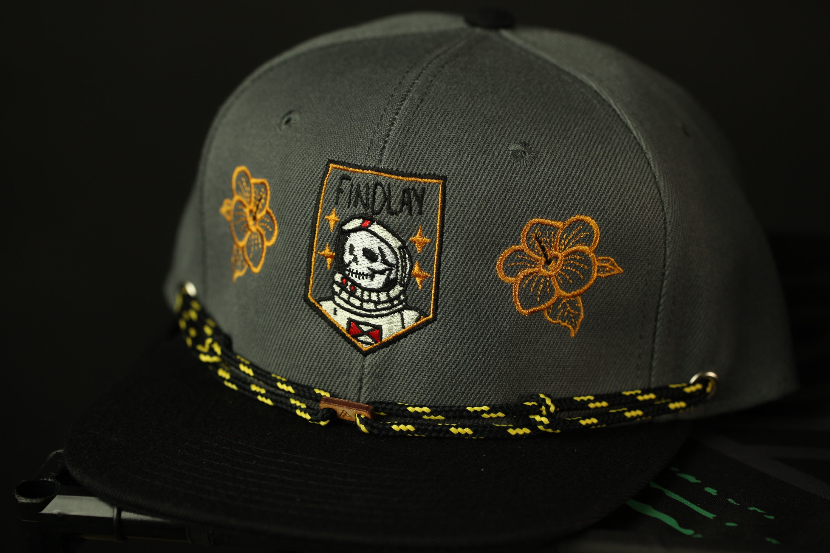 A gray baseball cap with a black brim and yellow floral designs on the front.