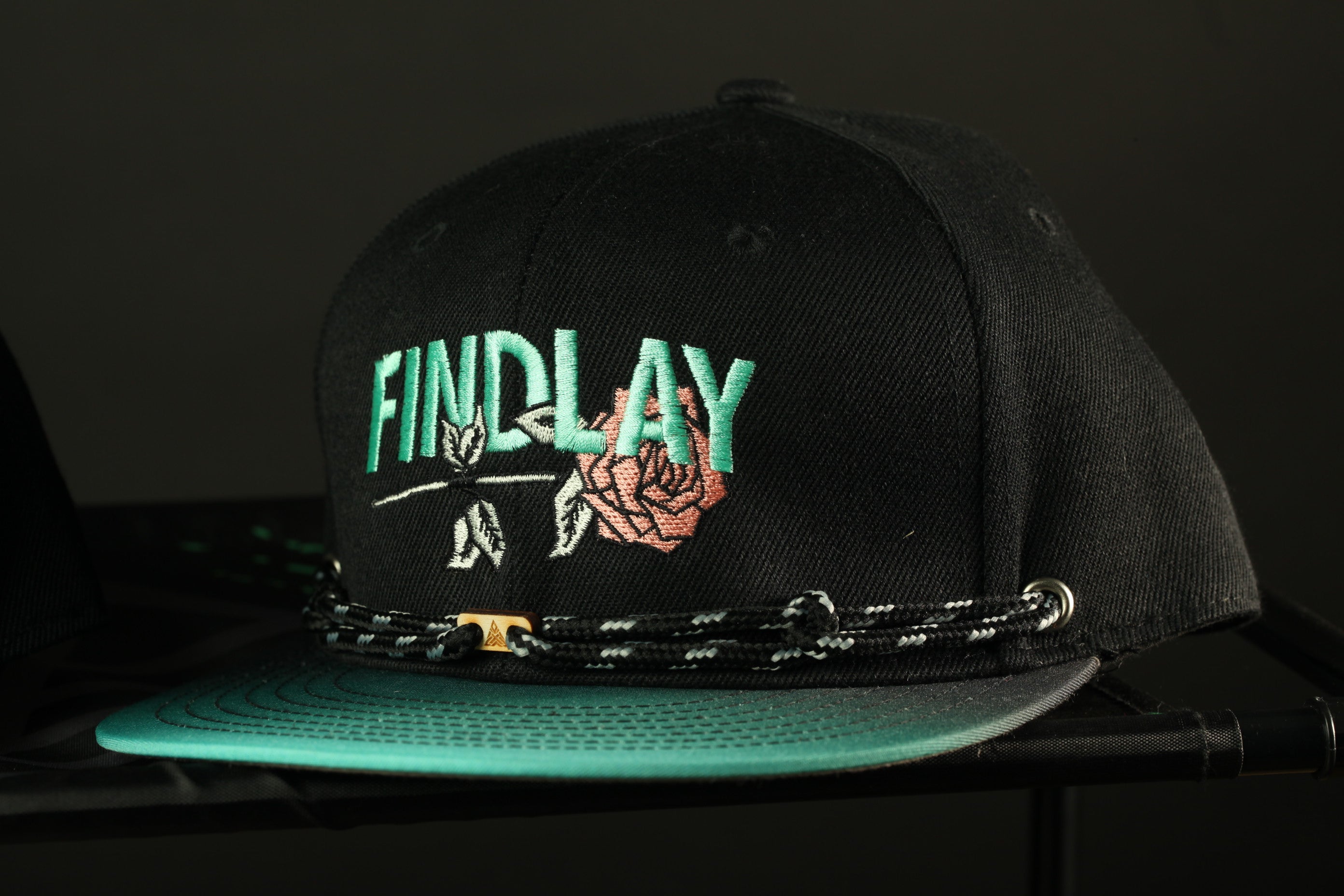 A black baseball cap with the word "FINDlay" embroidered on it, sitting on a black surface.