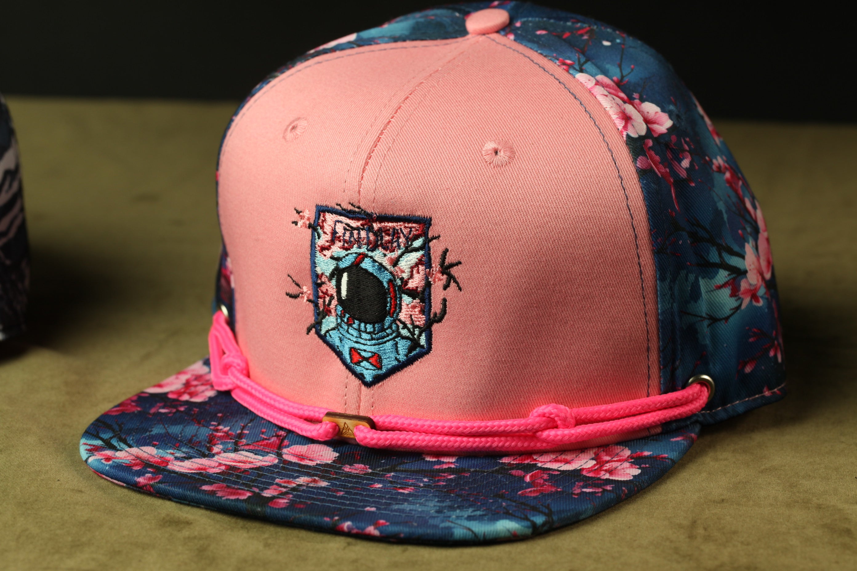 A pink baseball cap with a floral pattern and a small embroidered patch on the front.