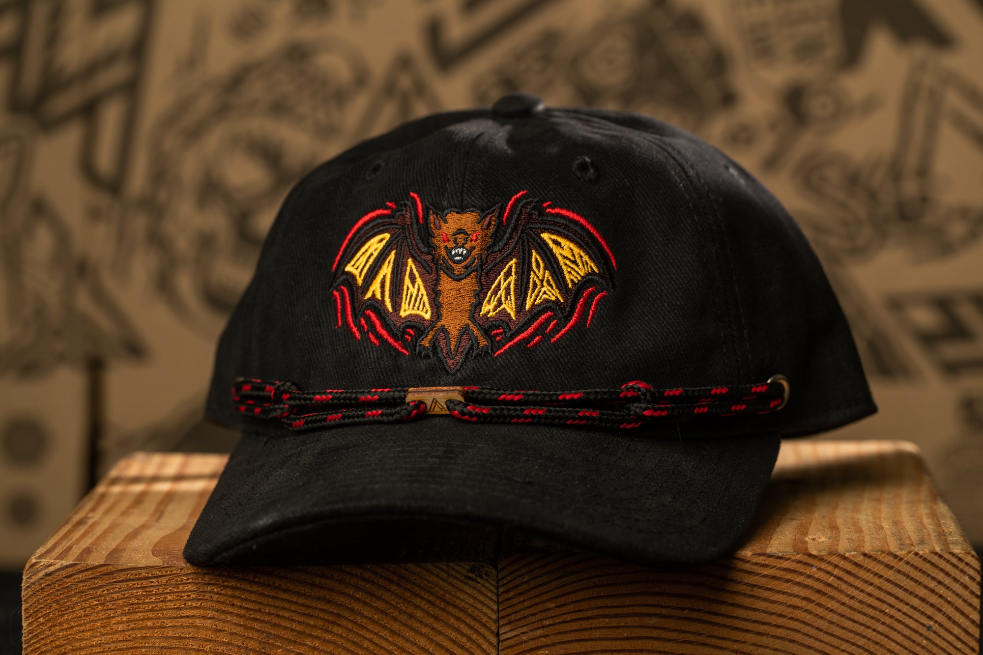 A black baseball cap with a bat design on the front, sitting on a wooden surface.
