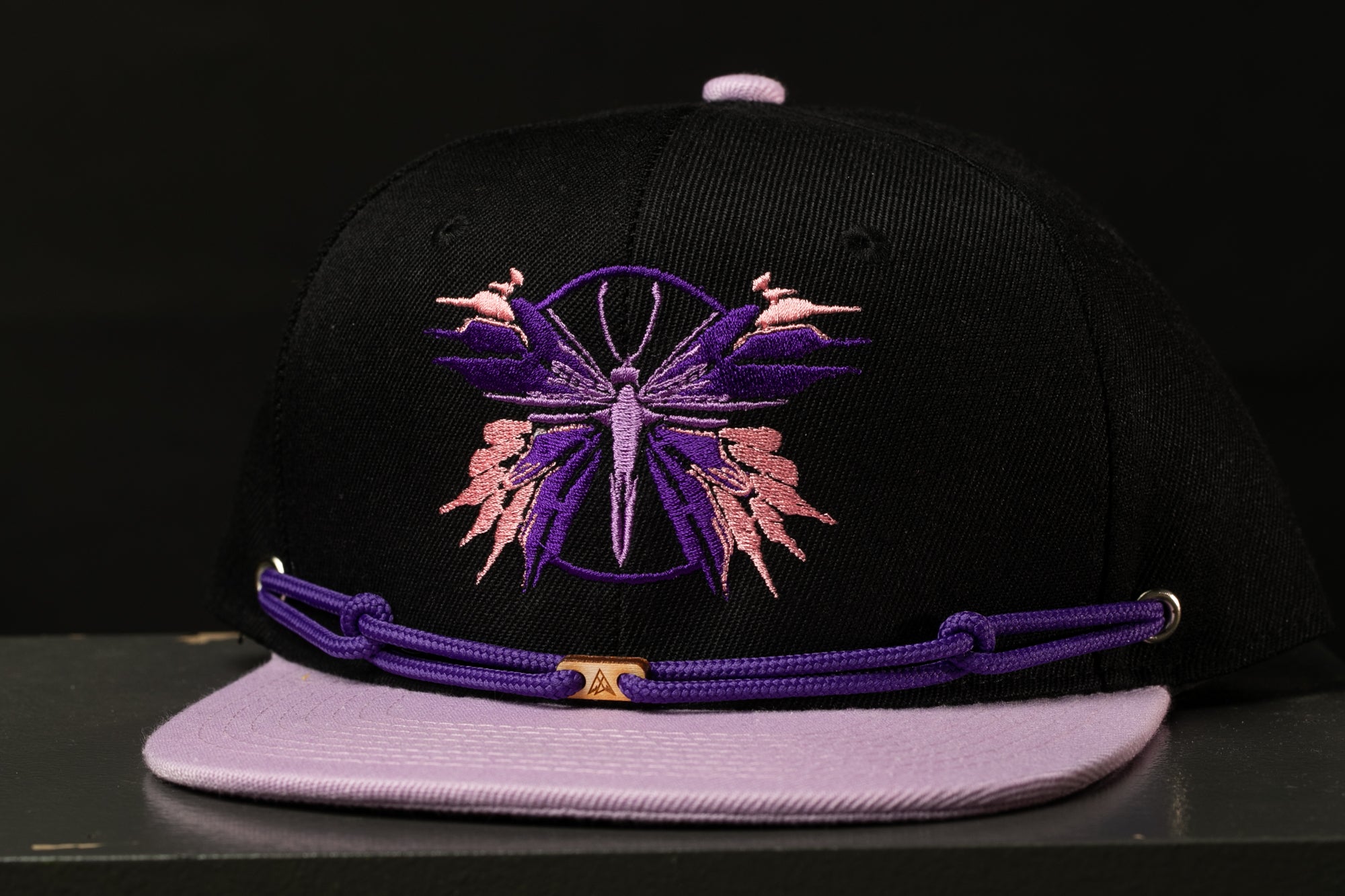 A black baseball cap with a purple and pink butterfly design on the front.