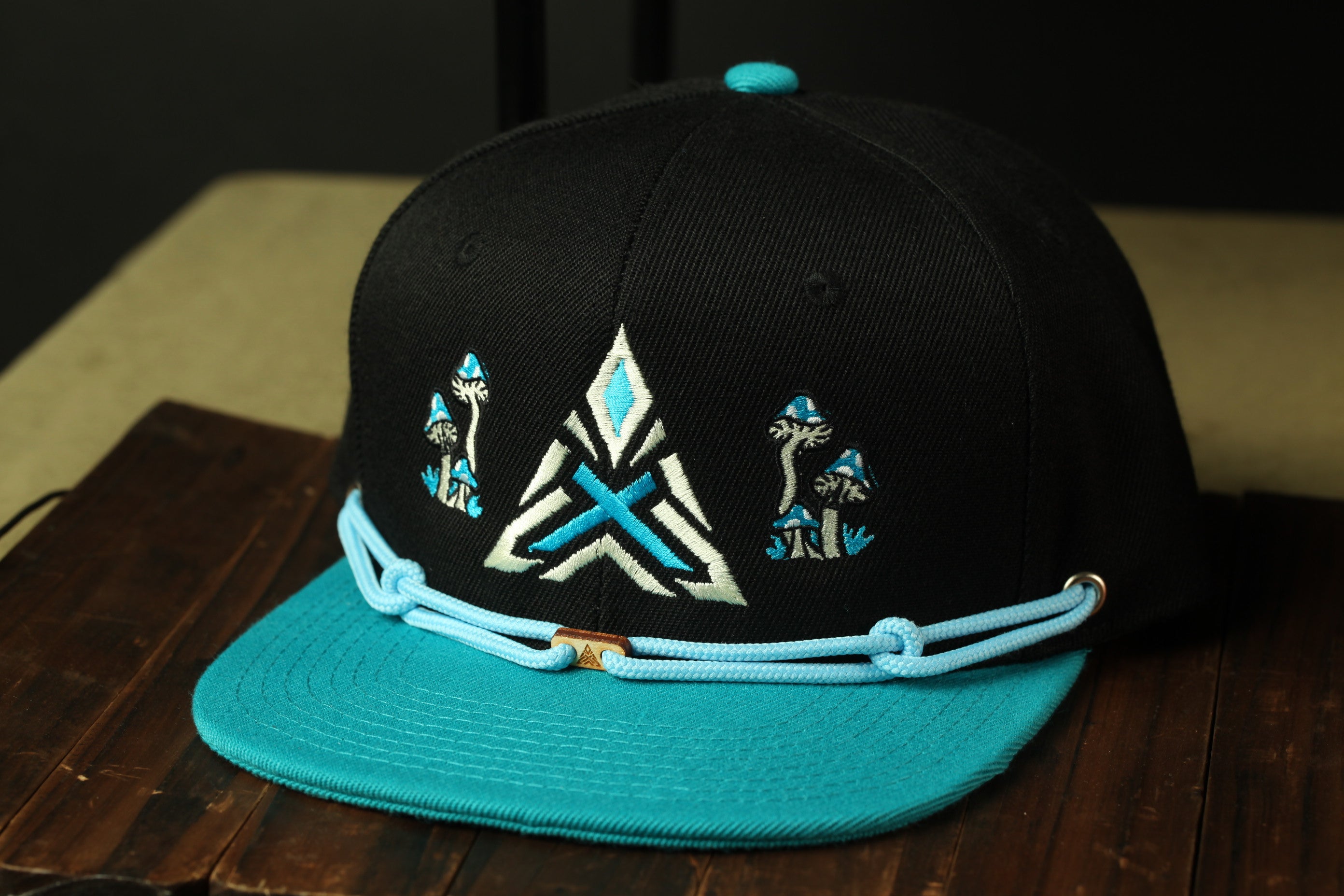 A black baseball cap with a teal brim and a blue-and-white geometric design on the front.