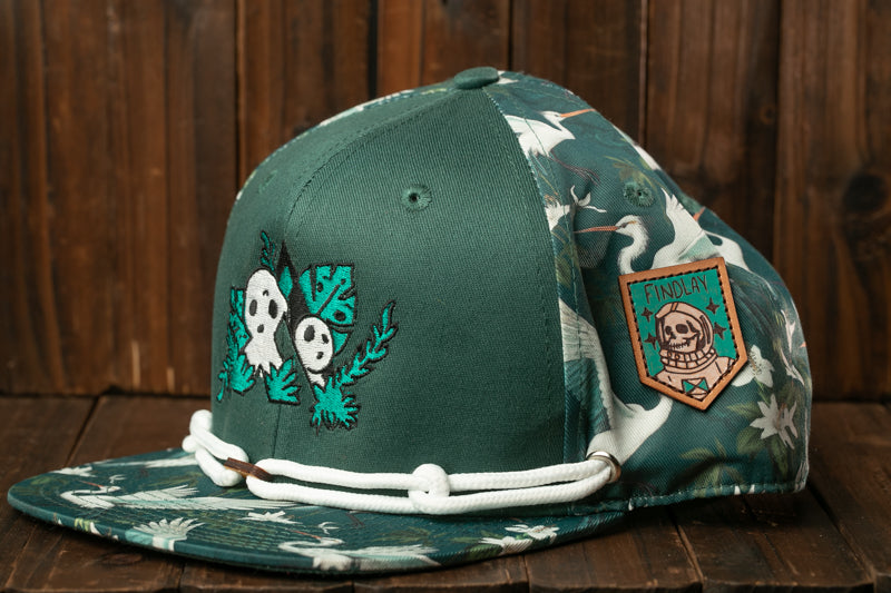 A green baseball cap with a floral pattern and a skull and crossbones design, placed on a wooden surface.