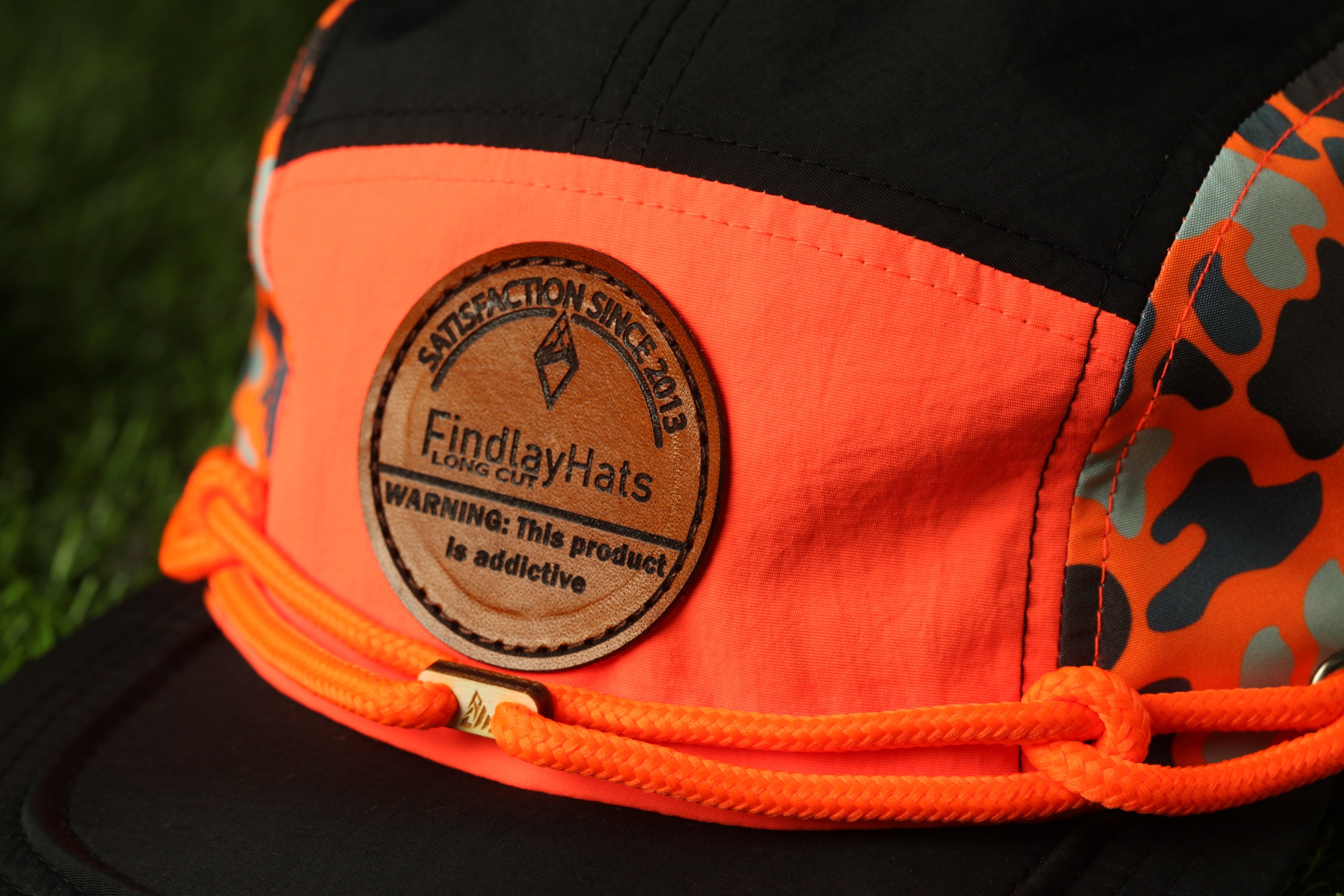 A close-up of a black and orange baseball cap with a leather patch on the front.