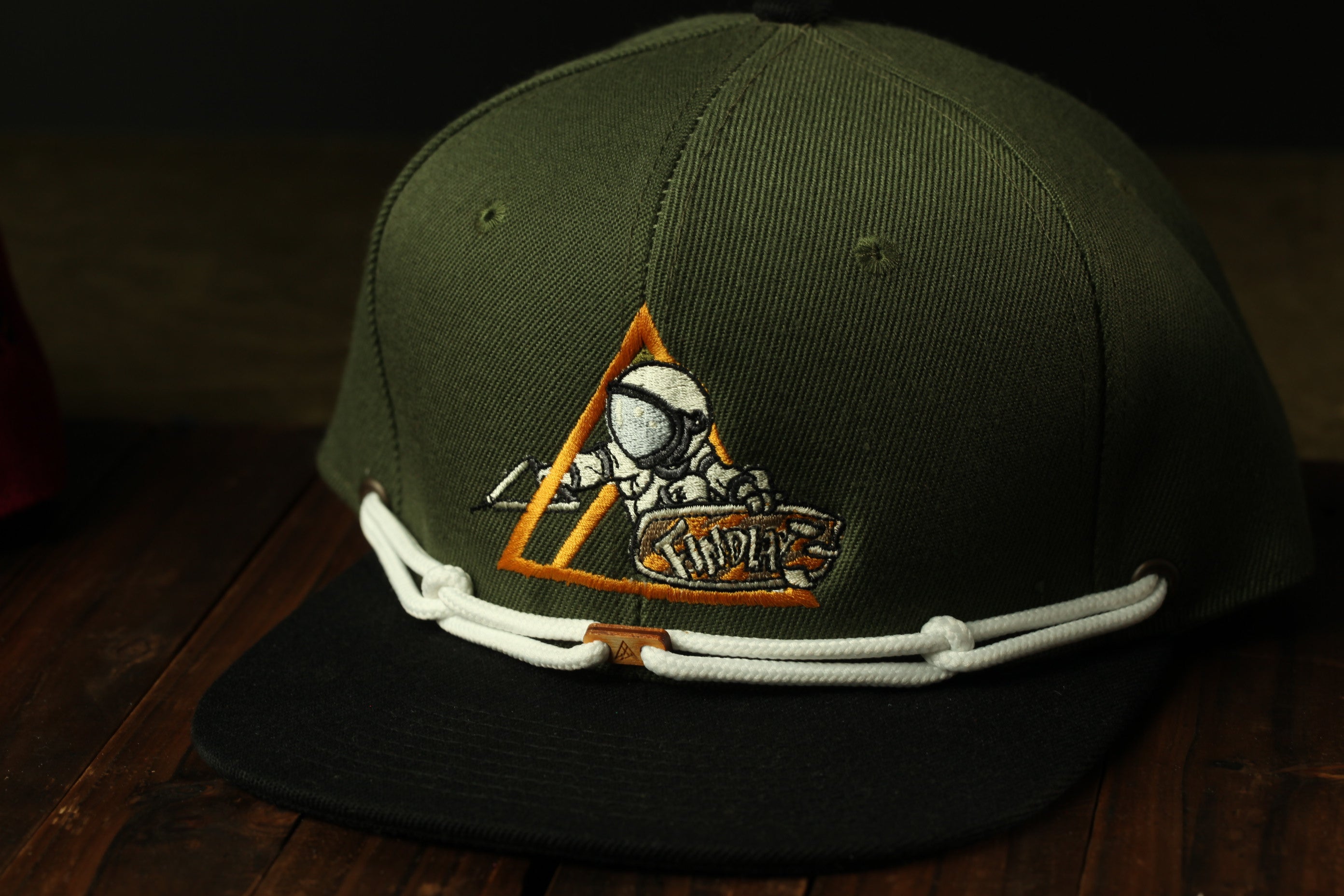 A green baseball cap with an orange triangle design and a graphic of a person riding a skateboard.