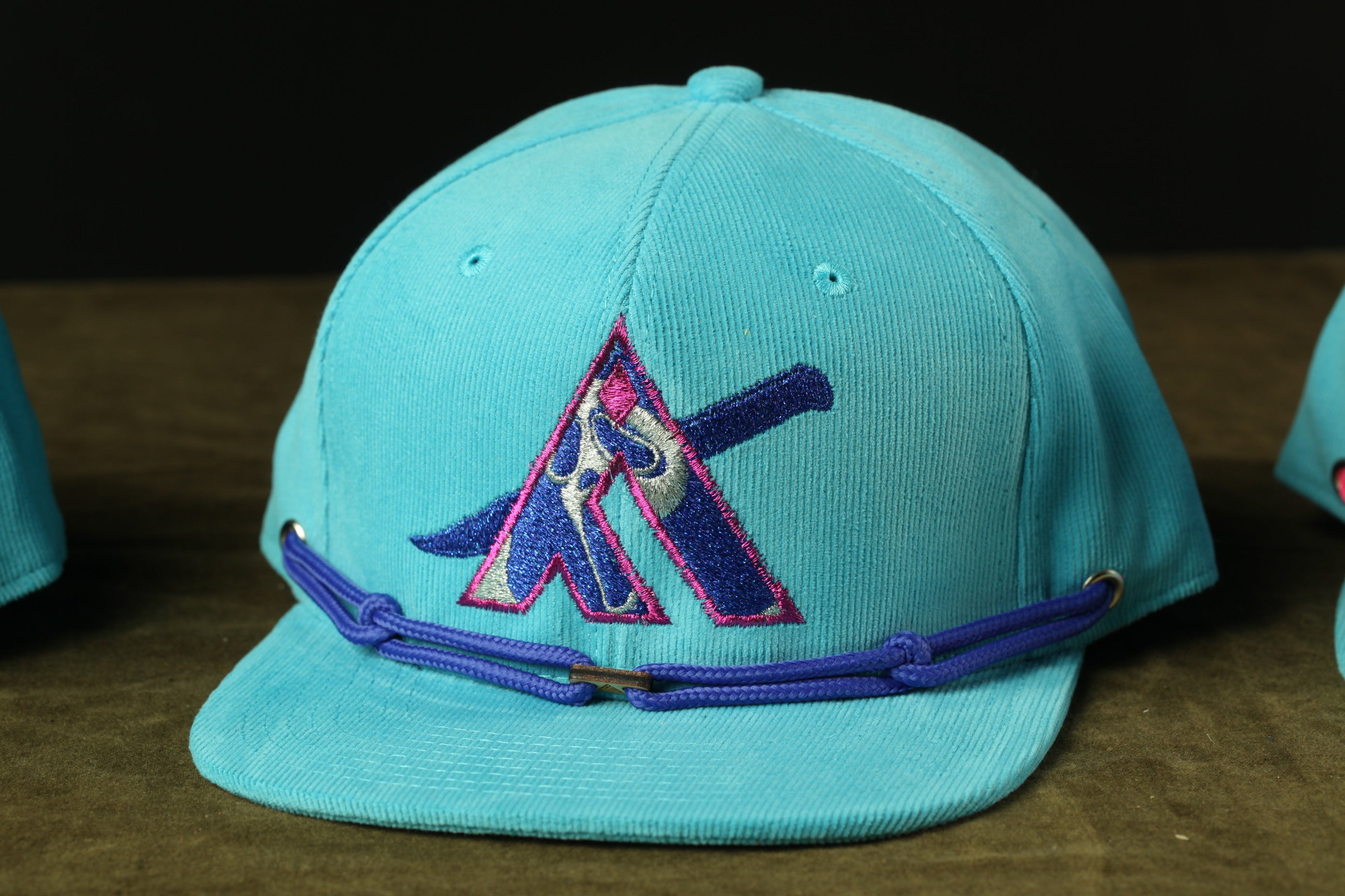 A turquoise baseball cap with a purple and blue logo on the front.