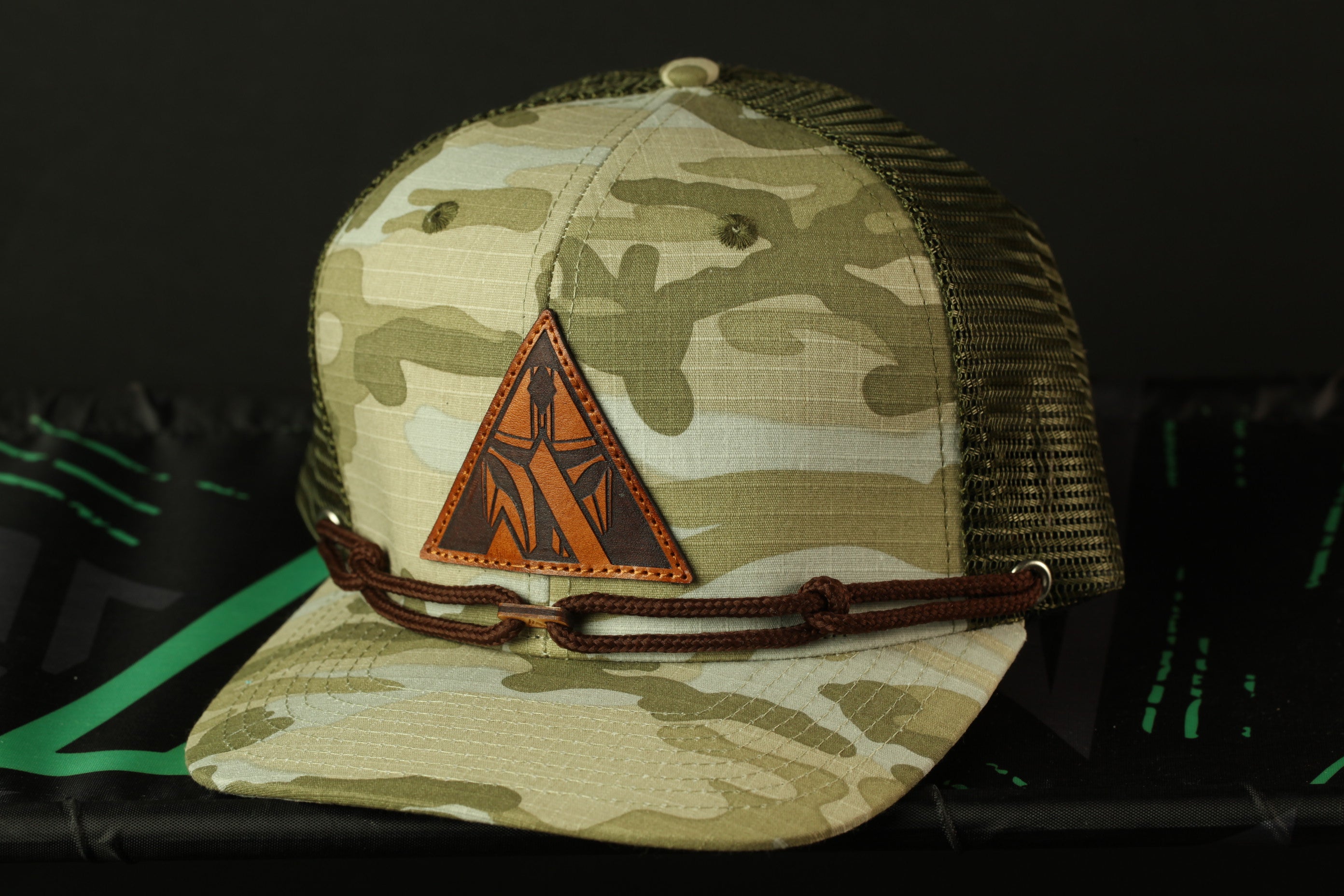 A camouflage baseball cap with a leather patch and a brown chain strap.