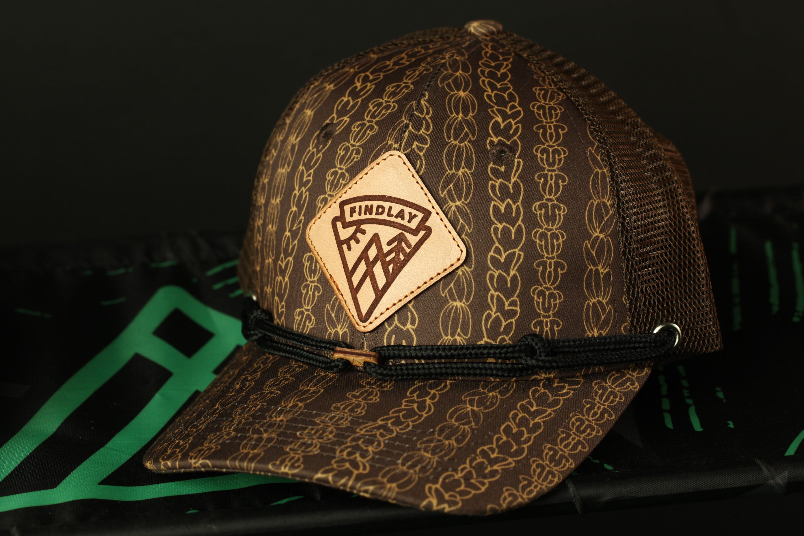 A brown baseball cap with a mesh back and a leather patch on the front, featuring a mountain design.