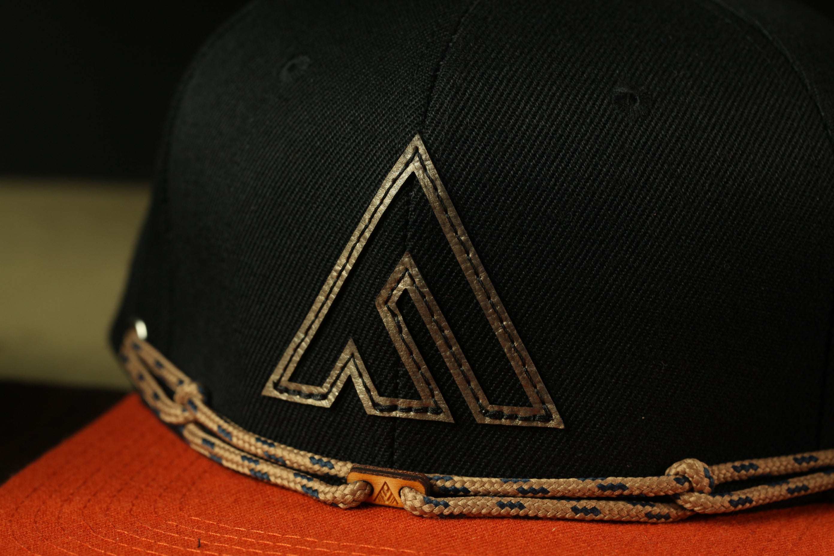 A close-up view of a black baseball cap with a gold-colored logo on the front.
