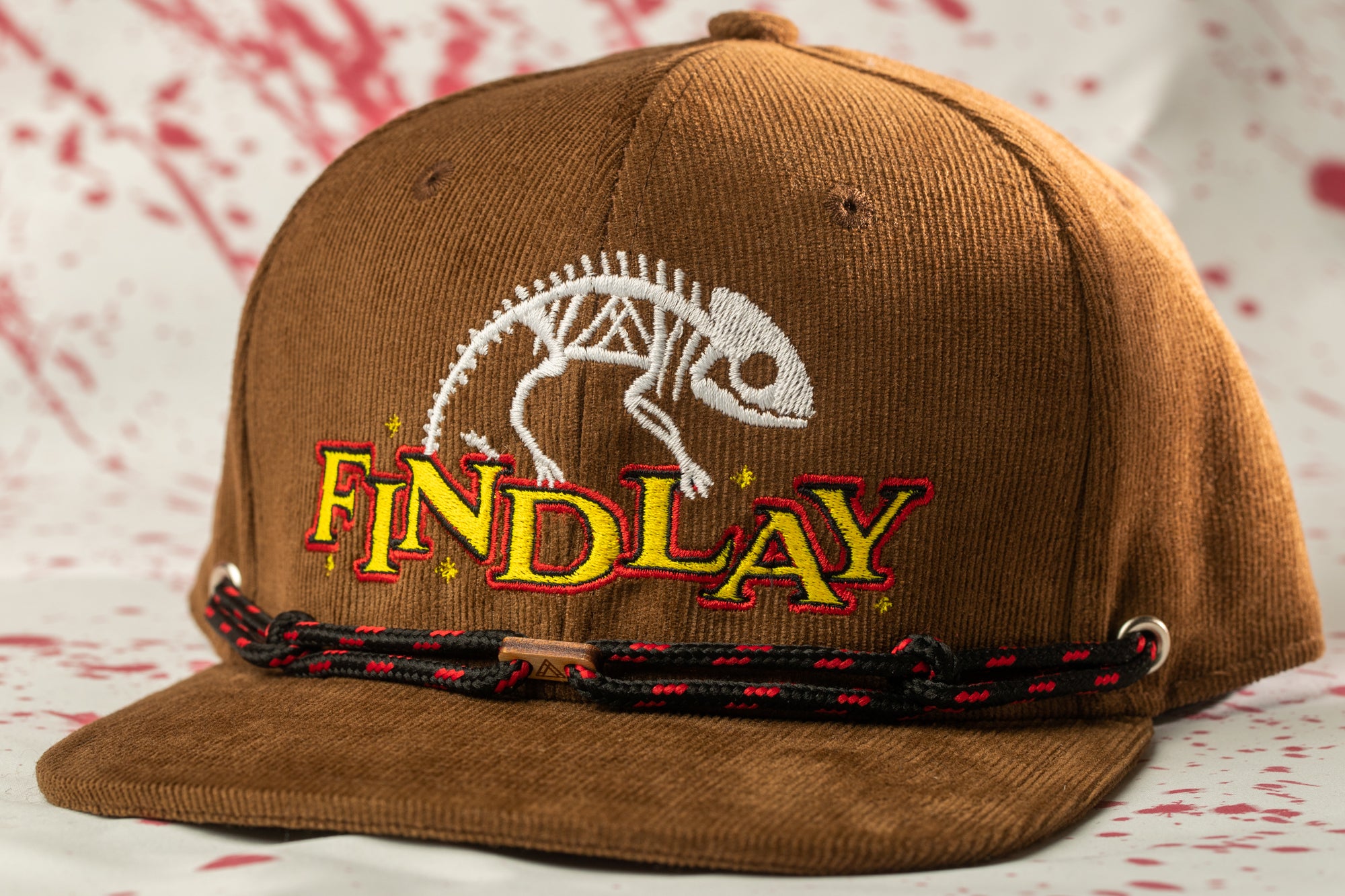 A brown baseball cap with a white and yellow logo and the word "FINDLAY" printed on it.