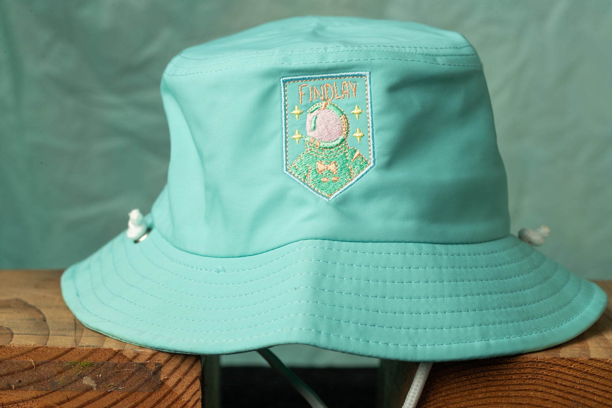A turquoise bucket hat with a patch on the front displaying the word "FAMOUS".