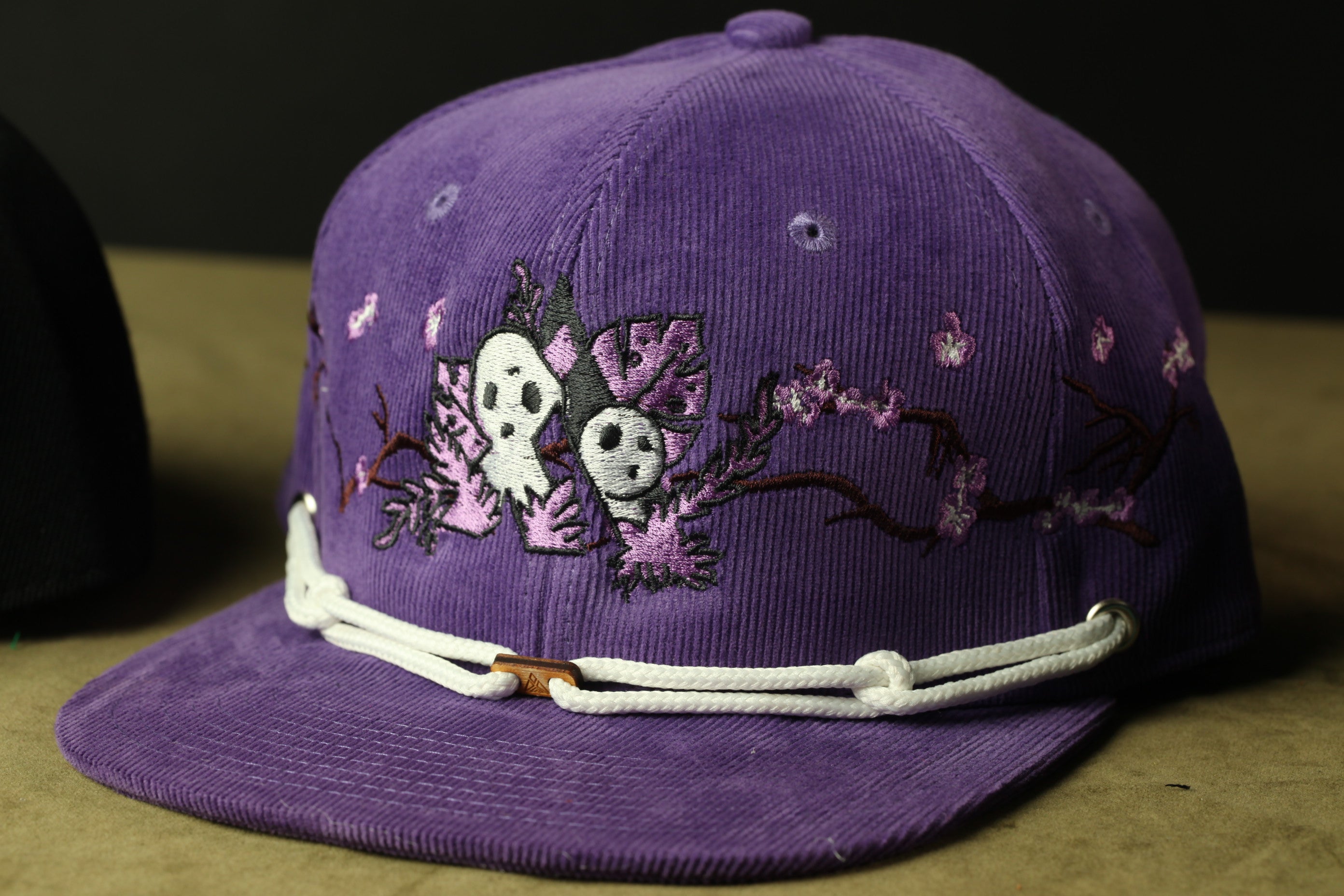A purple baseball cap with a floral design and two small white skulls on the front.