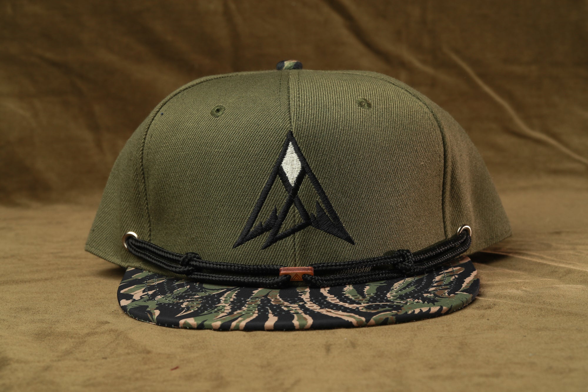 A green baseball cap with a camouflage pattern and a logo on the front, placed on a brown surface.
