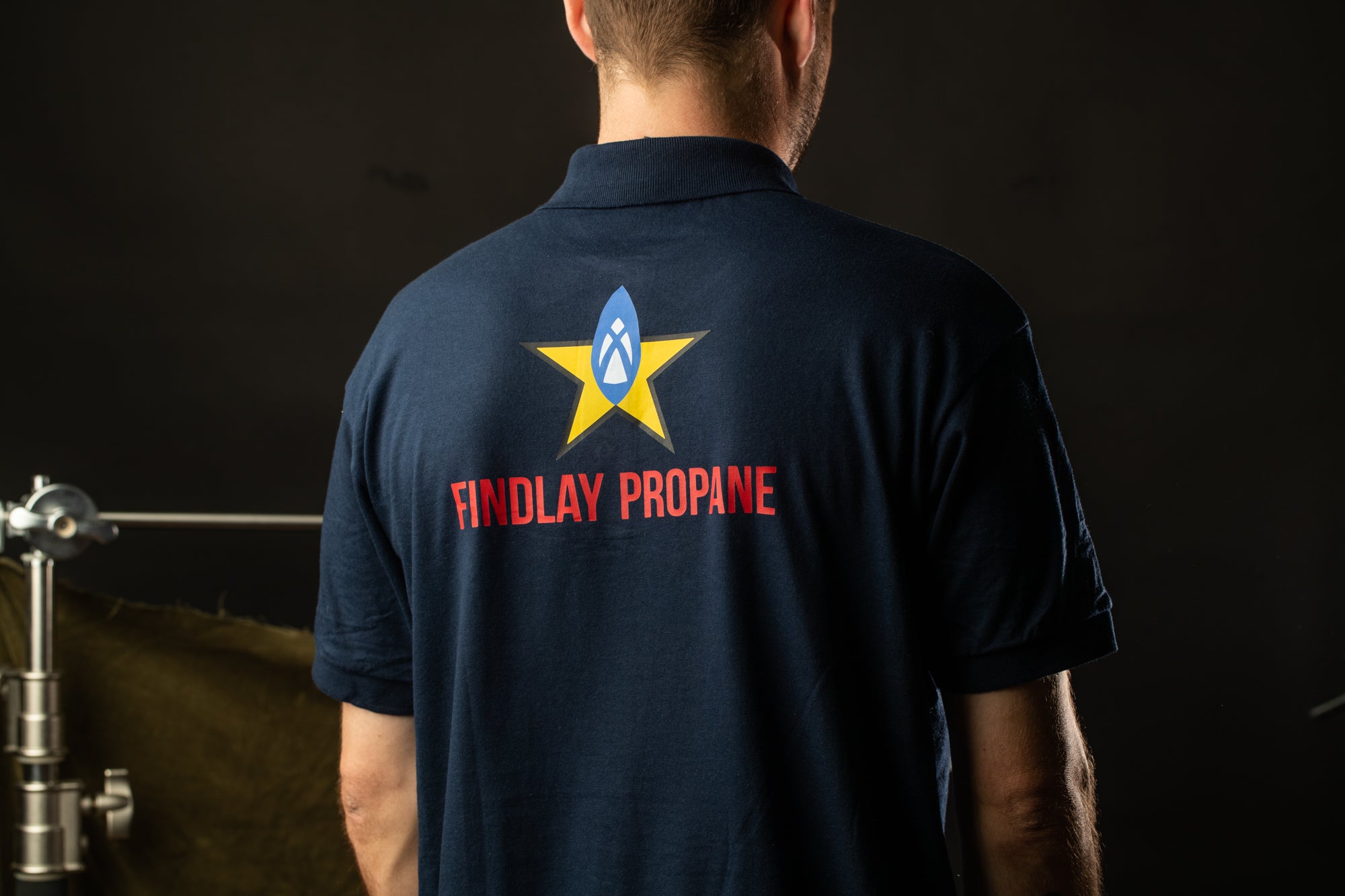 the back of a man wearing a navy blue polo shirt with the text "Findlay Propane" printed on it.