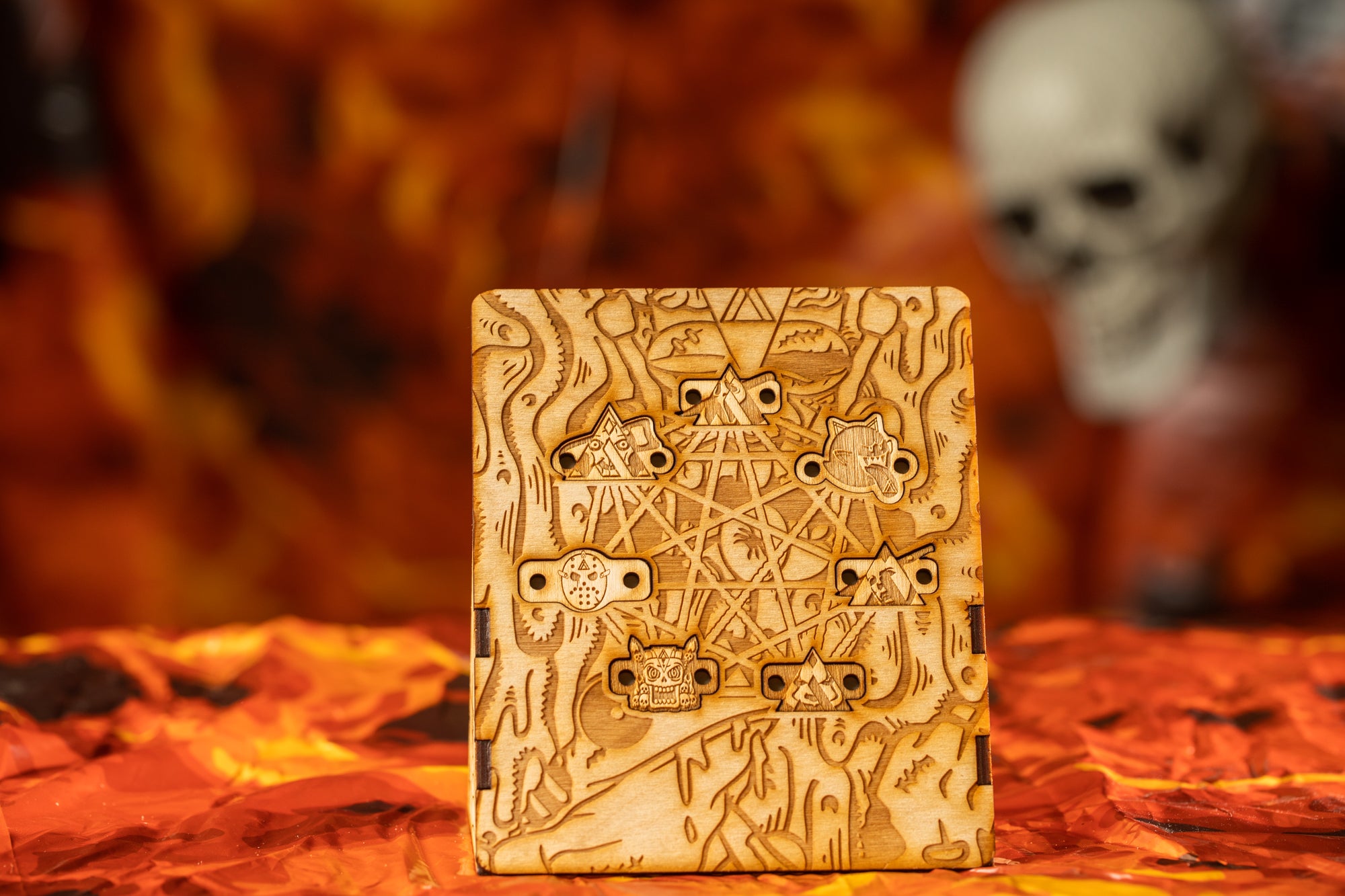 a wooden object with intricate carvings, including a skull and various symbols, set against a fiery orange background.