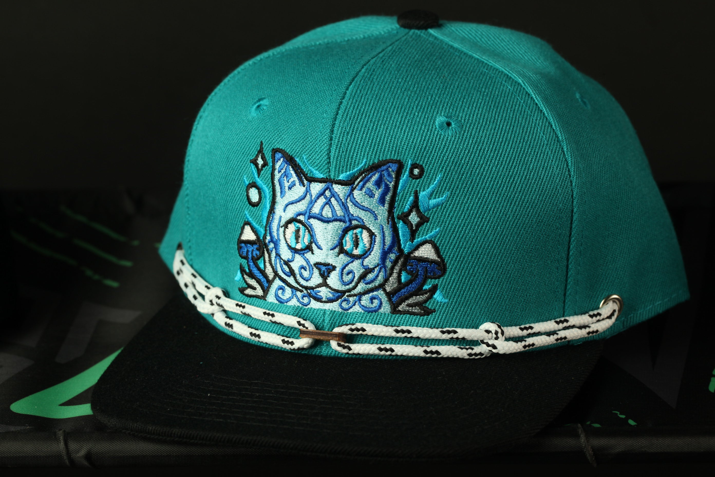 A turquoise baseball cap with a cat embroidered on it, featuring a black brim and white lace trim.