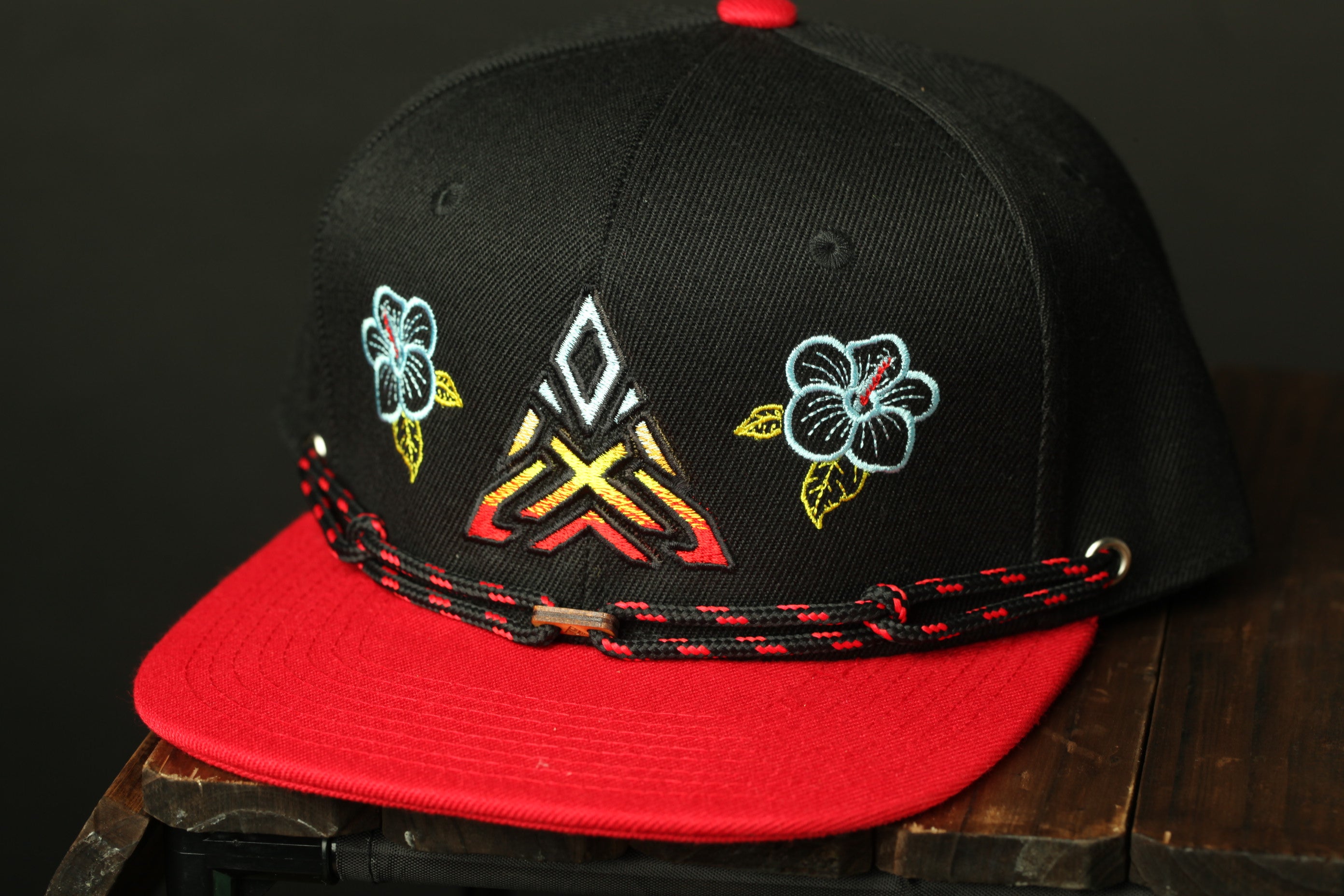 A black baseball cap with red trim and colorful floral designs on the front.