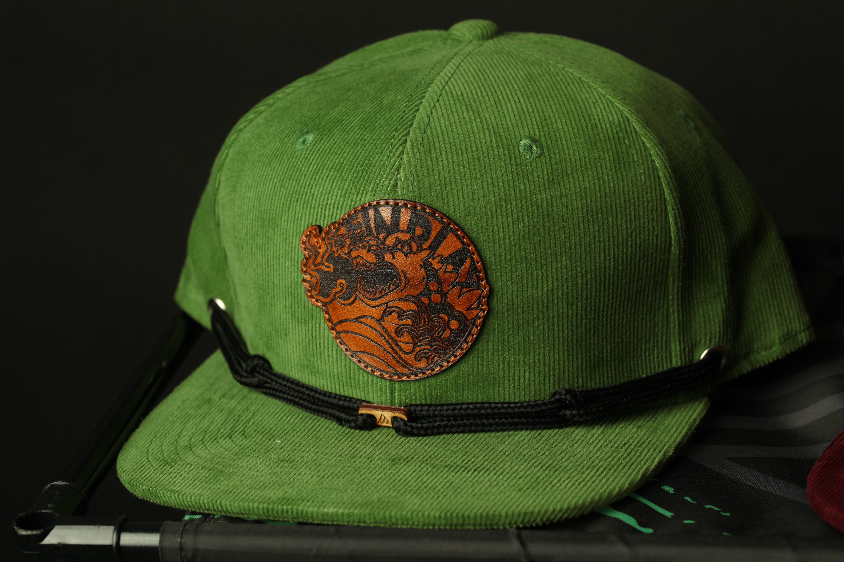 A green baseball cap with a leather patch featuring an intricate design.